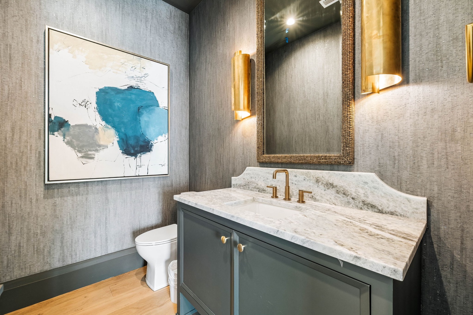Freshen up in this elegantly styled powder room featuring luxe marble countertops, sophisticated gold accents, and designer textured wallcovering that sets a refined, modern tone.