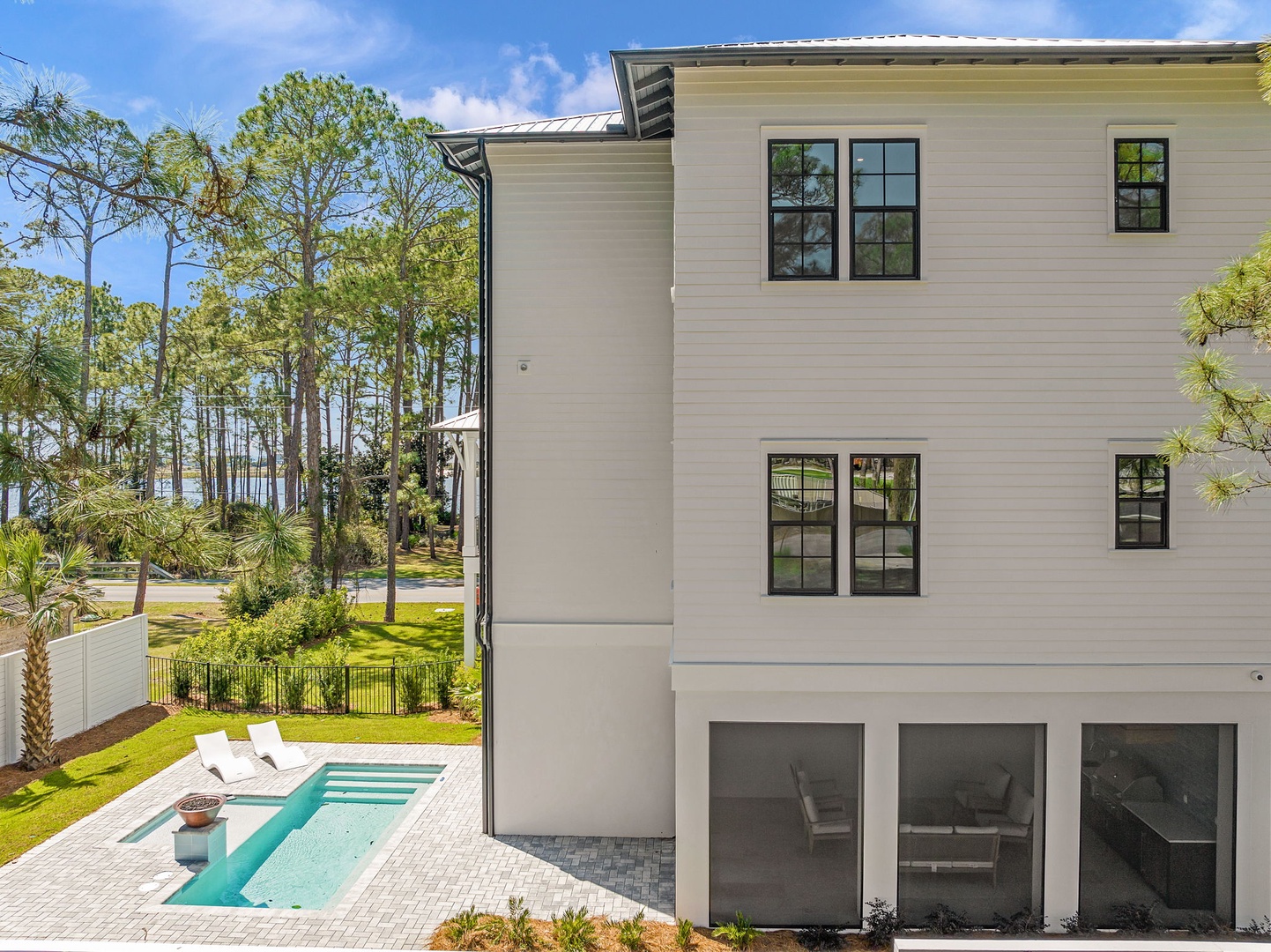 Modern three-story vacation home featuring a pristine pool and lush landscaped grounds surrounded by tropical palms.