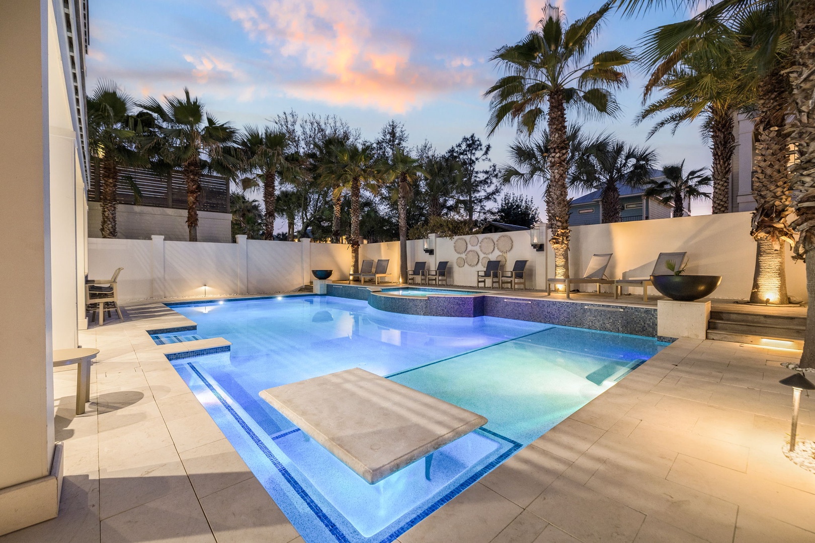 Dive into your private oasis with this stunning illuminated pool, surrounded by tropical palms and elegant lounging areas for perfect evening relaxation.