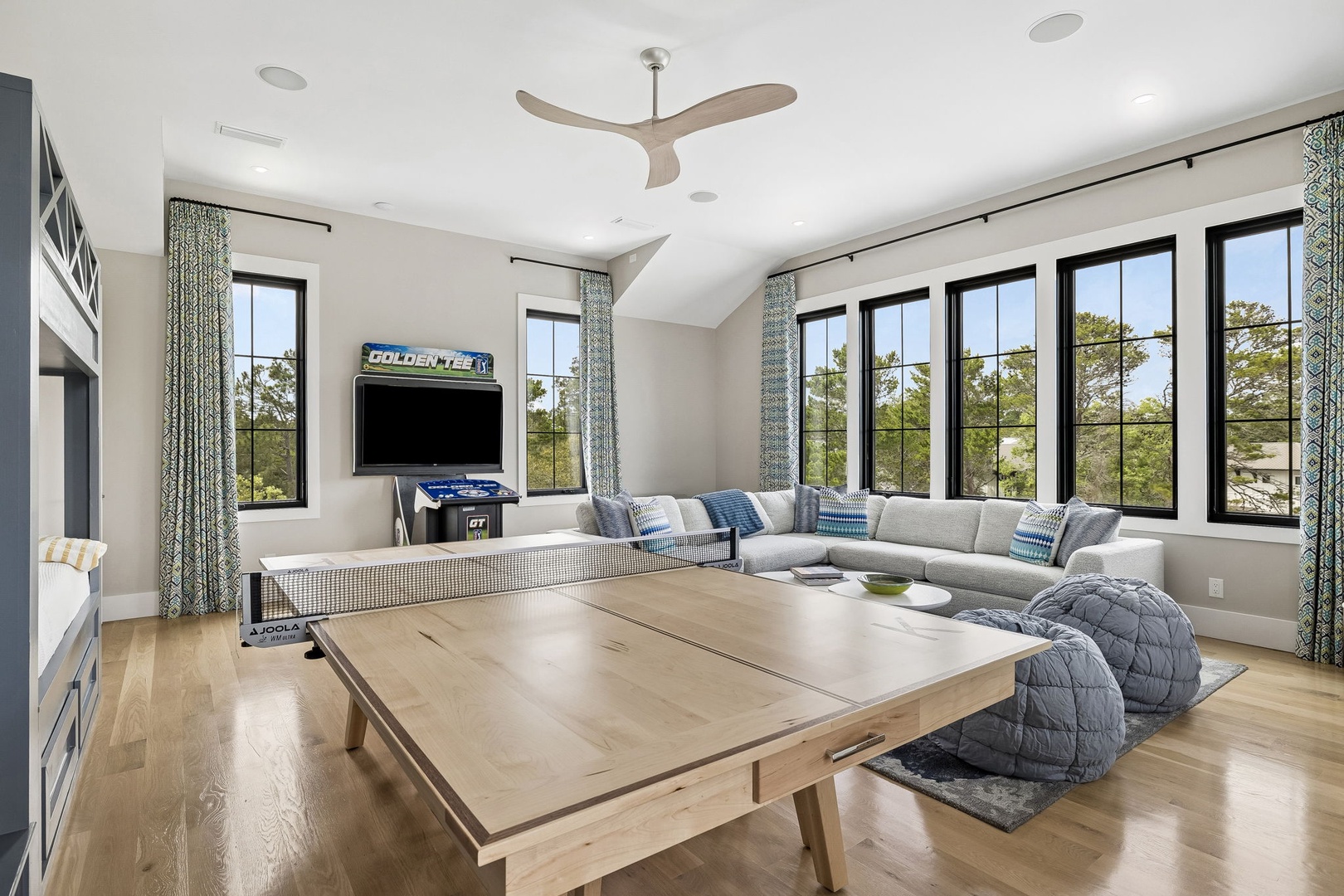 You'll love gathering here for friendly table tennis matches beneath soaring vaulted ceilings, or lounging on the plush sectional while natural light pours through floor-to-ceiling windows overlooking lush treetops.