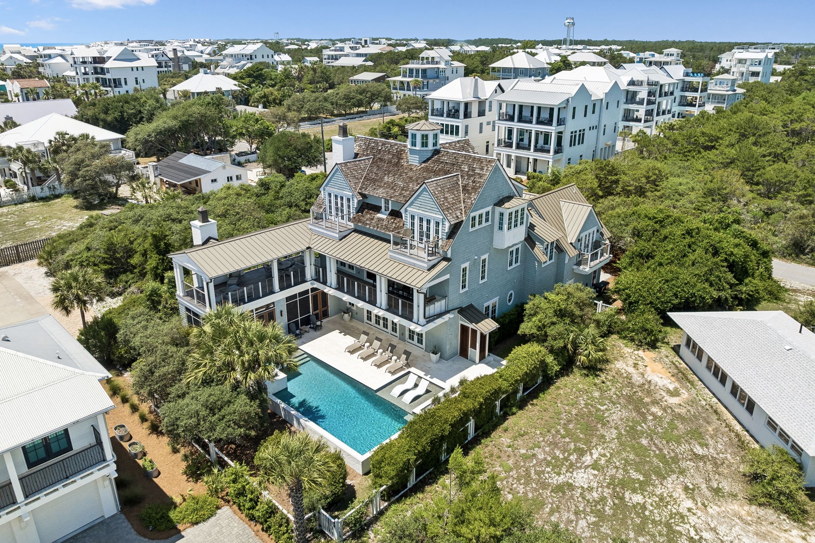 Aerial view of a spacious coastal vacation home featuring a private pool, lush landscaping, and elegant coastal architecture within a prestigious beachside community.