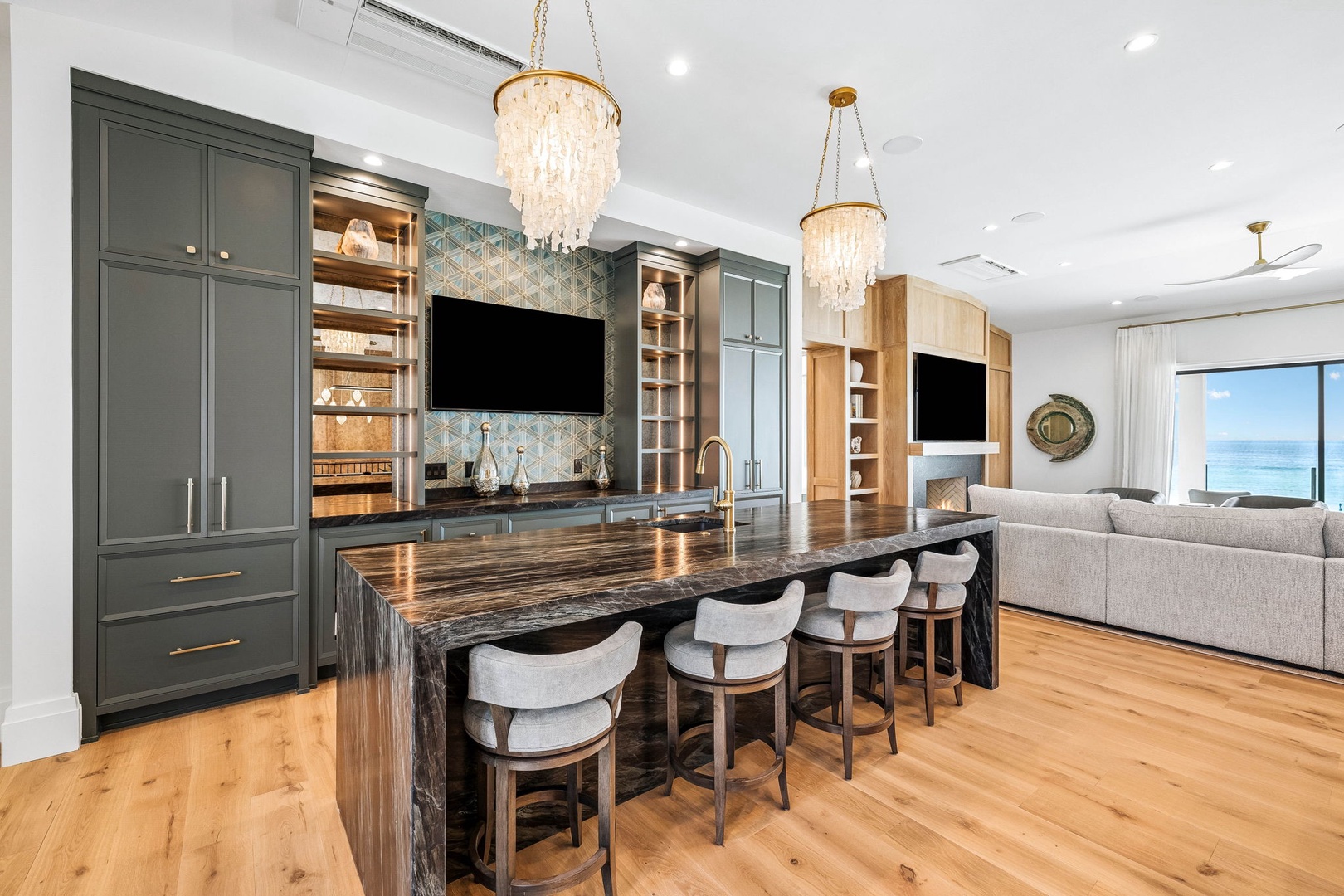 Gather around the elegant island with bar seating, where chandeliers cast a warm glow and stunning ocean views invite you to unwind in style.