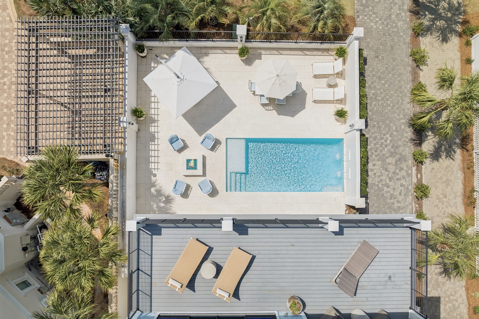 This aerial view showcases the property's stunning pool area and rooftop terrace, surrounded by tropical palm trees in a peaceful residential setting.