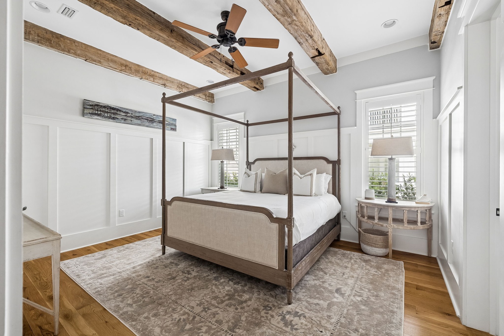 Step into your serene bedroom retreat, where rustic wooden beams frame crisp white ceilings and a luxurious canopy bed promises restful nights. Natural light pours through plantation shutters, highlighting warm hardwood floors beneath your feet.