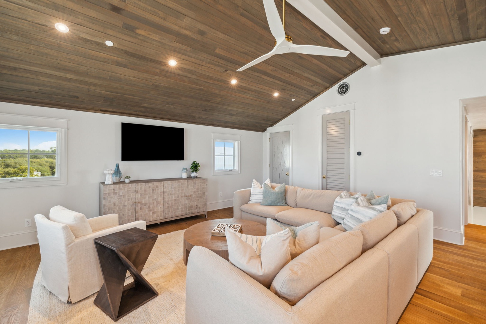 Sink into plush seating beneath soaring wood-paneled ceilings, where natural light and modern comfort create your perfect retreat for movie nights or cozy conversations.