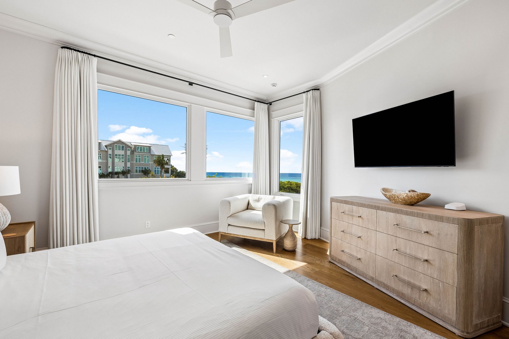 Wake up to stunning ocean views from your serene bedroom retreat. Light floods through expansive windows while ceiling fan keeps you comfortable. The coastal vista and nearby architecture create a picture-perfect backdrop for your stay.