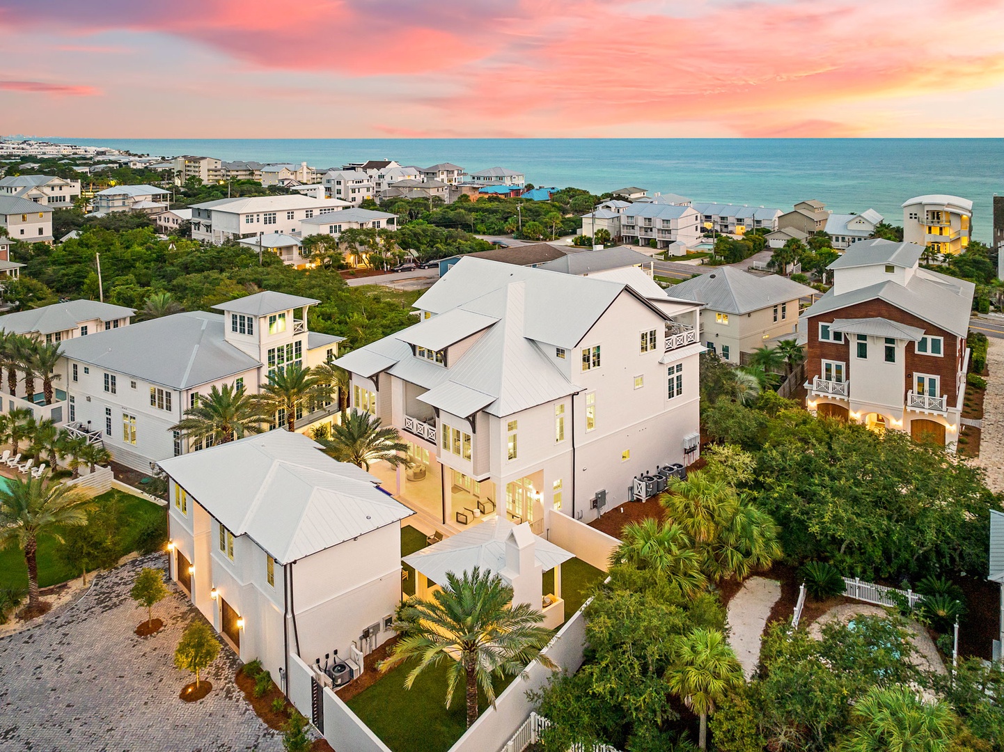 An expansive coastal property nestled among palm trees and lush landscaping, situated just steps from the ocean in a serene beachside neighborhood at sunset.