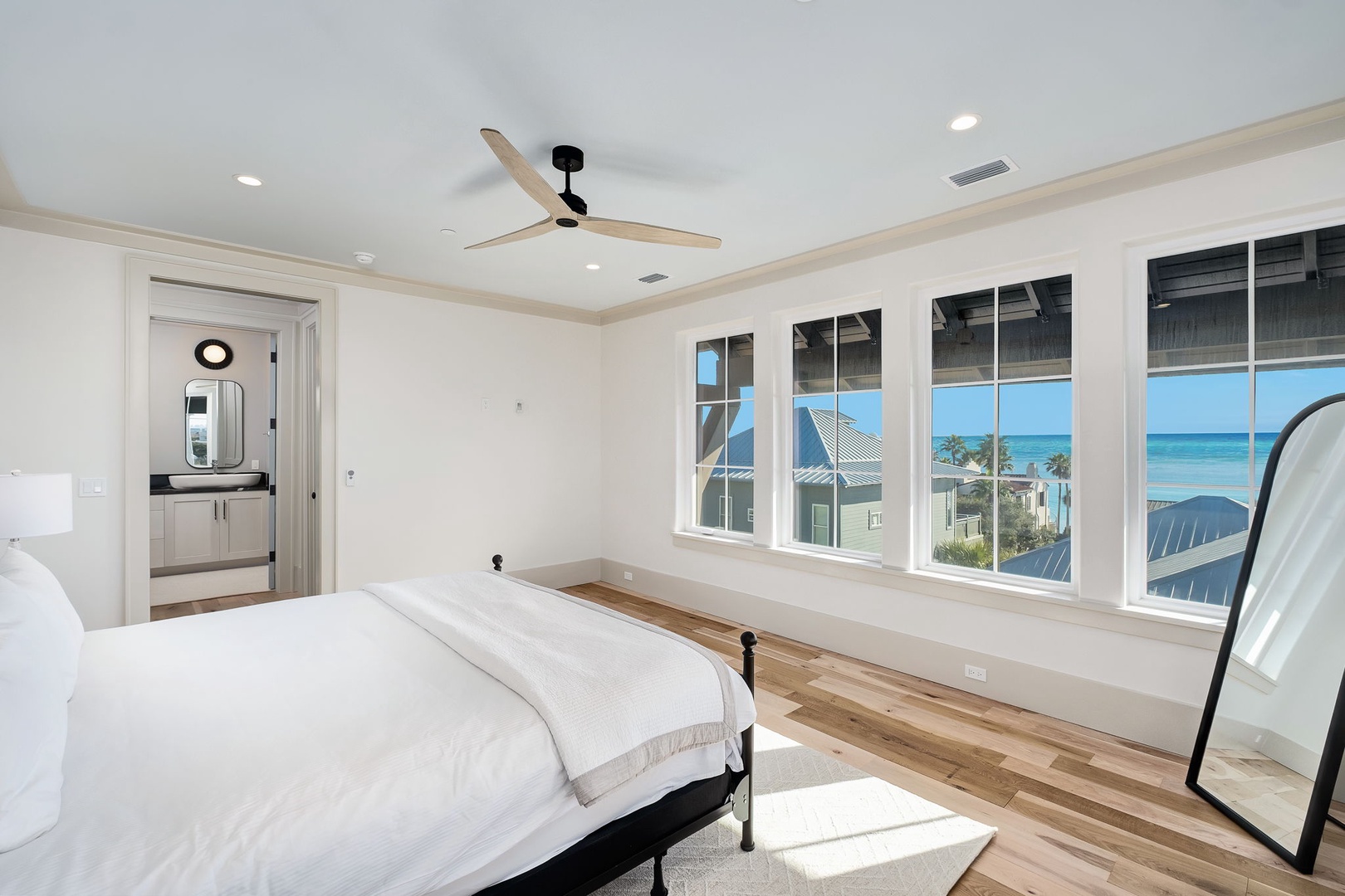 Your bright bedroom sanctuary features stunning ocean views through expansive windows, where gentle sea breezes flow beneath the ceiling fan.