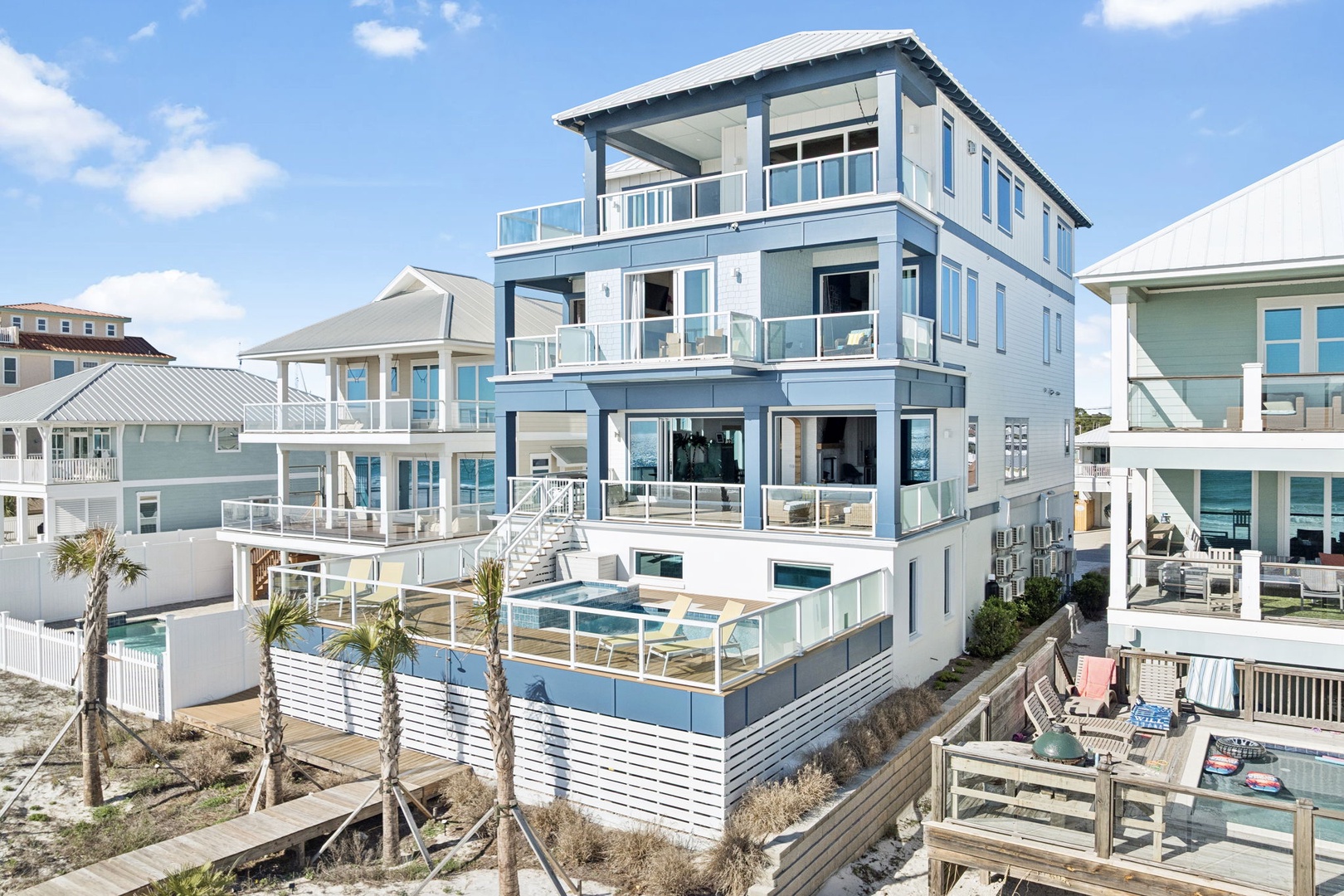 Modern three-story beachfront property featuring multiple balconies and a private pool, nestled among coastal palms in a vibrant beach community.