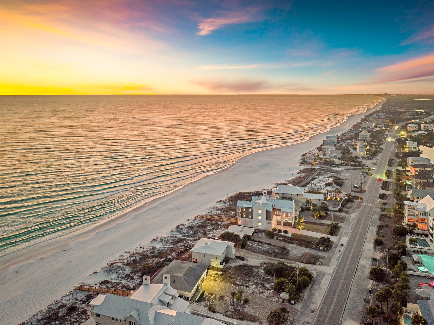 Stunning aerial view of beachfront properties along pristine white sand coastline at sunset, showcasing the scenic neighborhood setting.