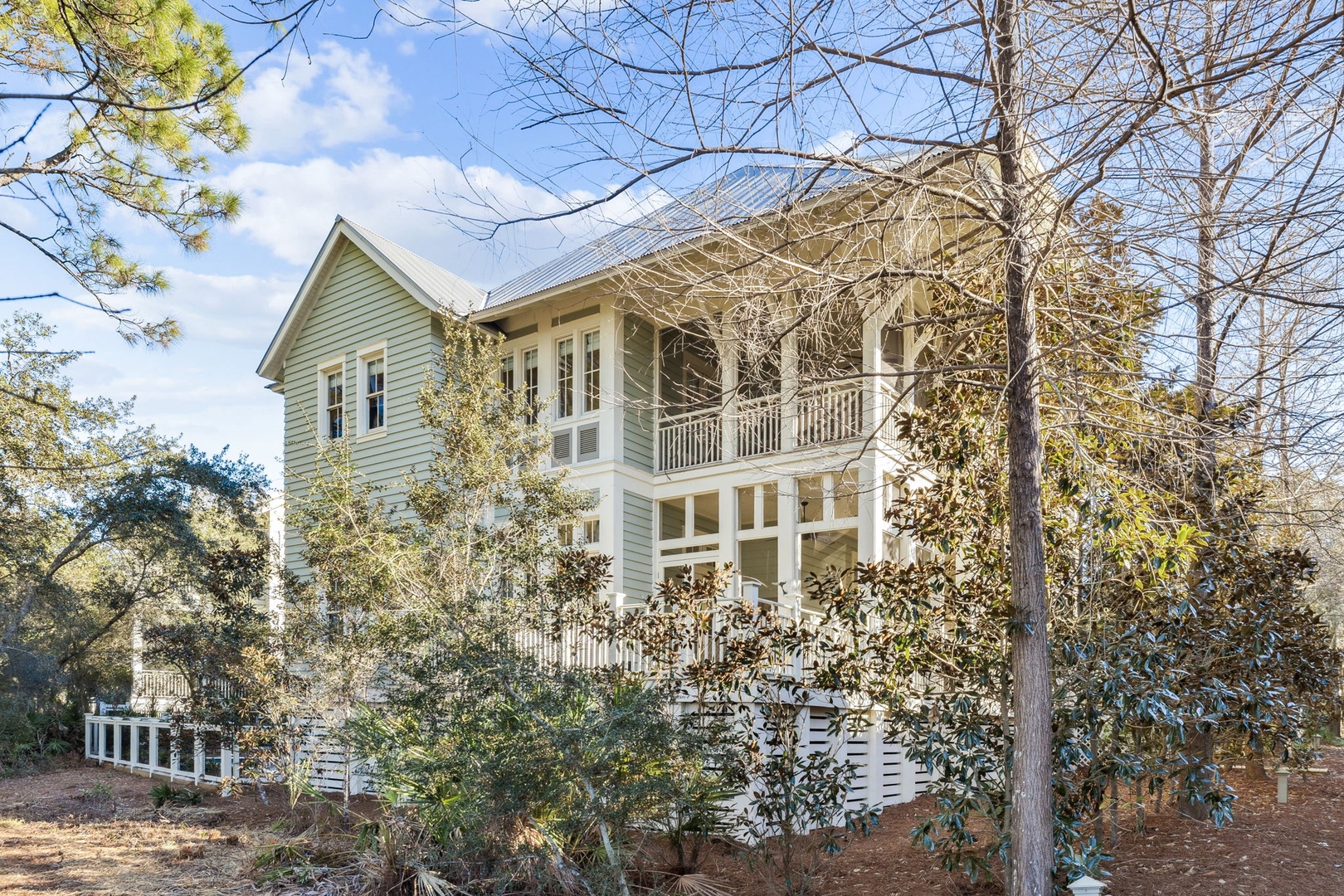 Charming two-story cottage nestled among mature trees, featuring classic architecture with wraparound porches and peaceful wooded surroundings.