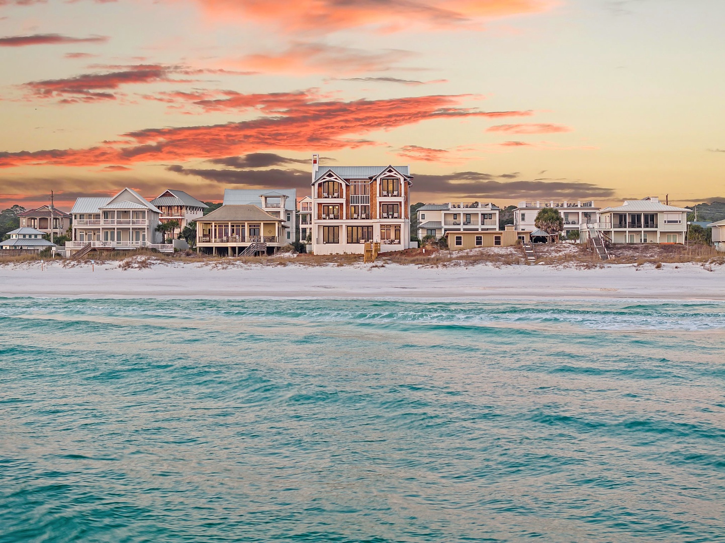 Stunning beachfront properties line pristine white sand shores with turquoise waters under dramatic sunset skies.