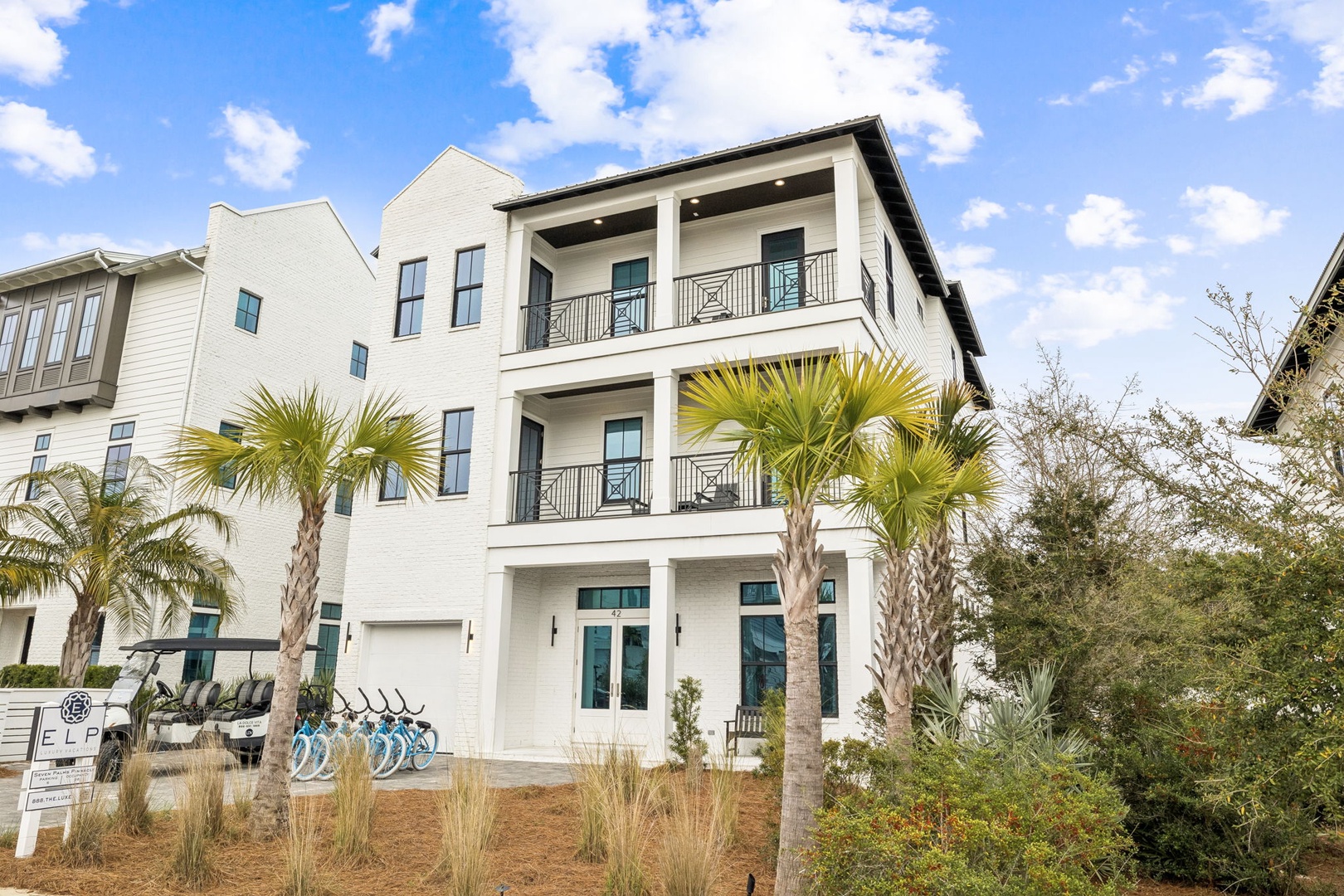 Modern three-story coastal home featuring multiple balconies and tropical palm landscaping in a peaceful residential neighborhood.
