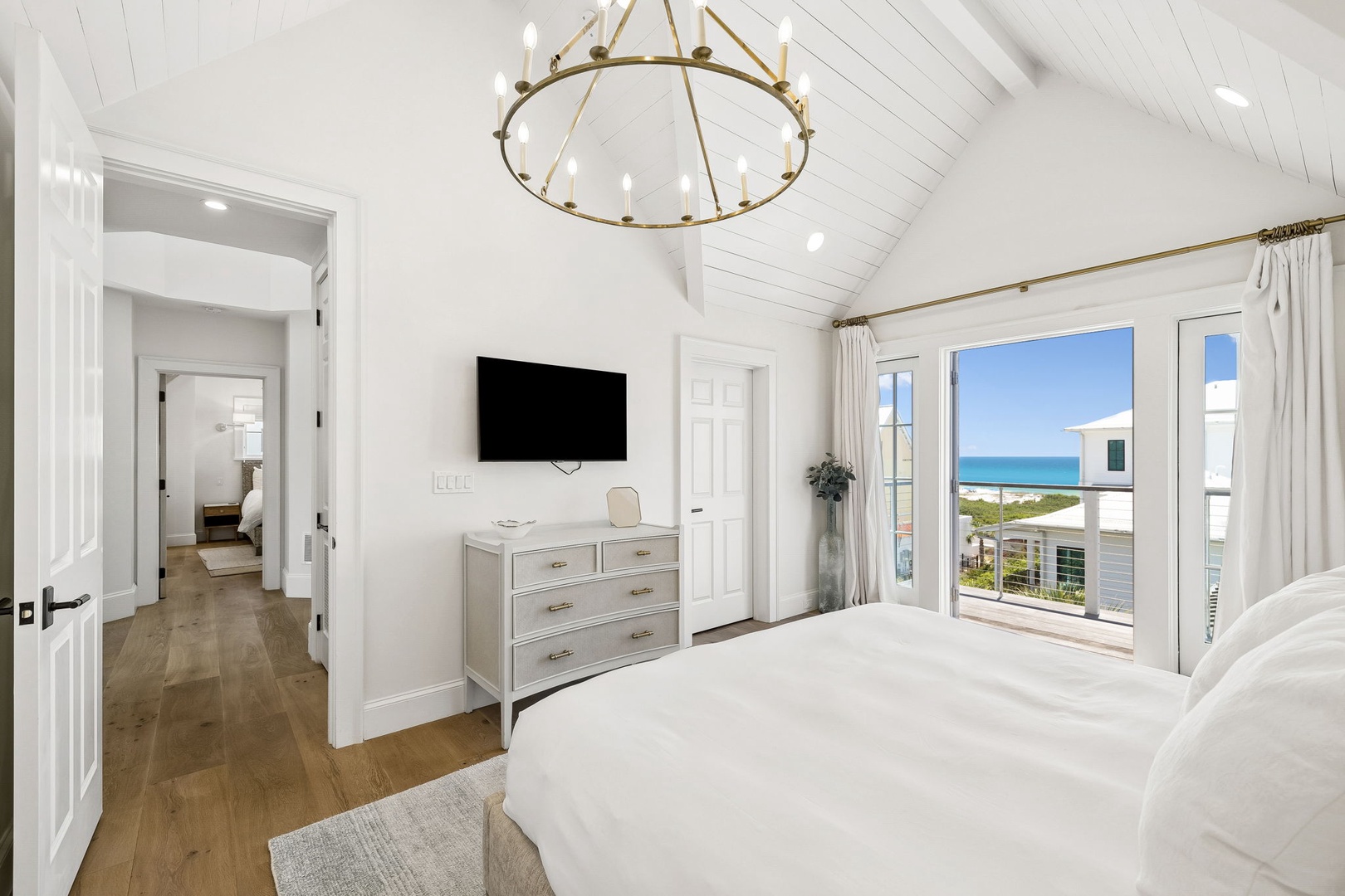 Wake up to stunning ocean views through expansive French doors opening onto your private balcony. The vaulted shiplap ceiling, elegant chandelier, and soft coastal tones create a serene retreat where you can unwind in style.