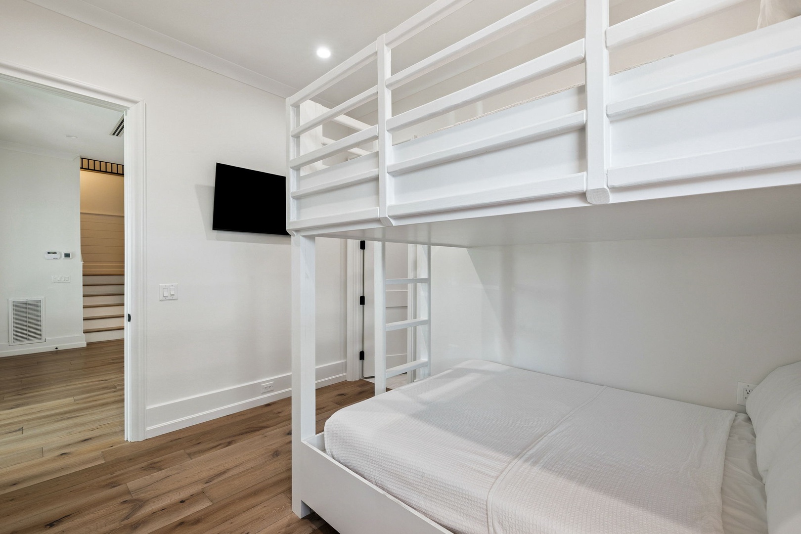 Your spacious bedroom features modern bunk beds with crisp white linens and a wall-mounted TV for cozy viewing nights.