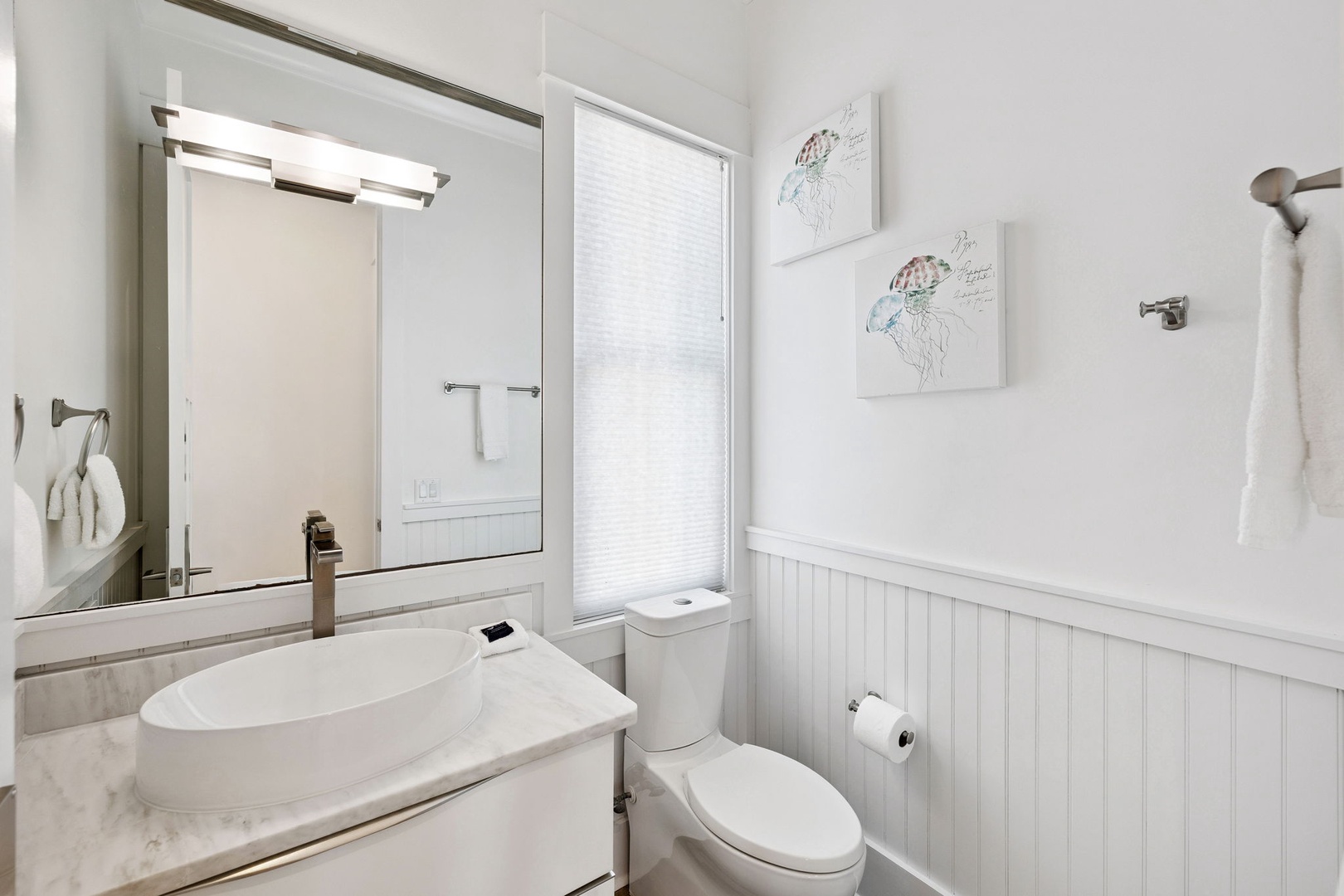 Your elegant powder room combines marble countertops with charming white wainscoting and thoughtful artwork for a refined yet welcoming atmosphere.
