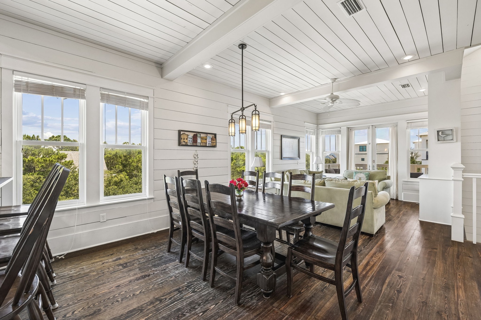 Gather around this spacious dining table where your family meals come with a side of coastal charm. Natural light floods in through large windows, framing lush greenery and inviting you to linger over breakfast or toast to another perfect beach day.