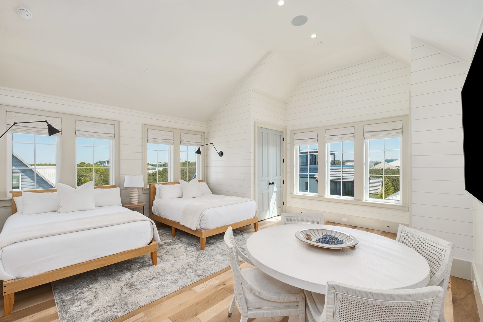 Your bright coastal bedroom features two comfortable beds, natural wood floors, and stunning windows that frame peaceful neighborhood views.