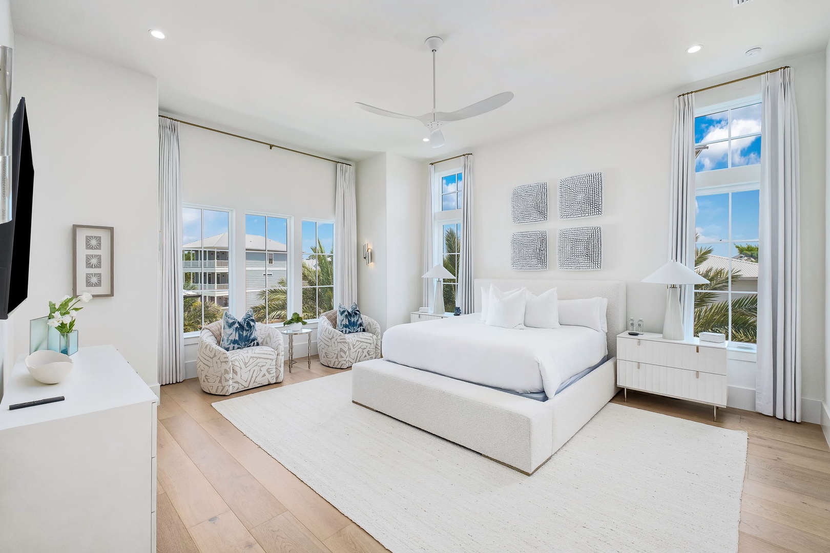 Sink into a cloud-soft king bed surrounded by coastal elegance and natural light. Floor-to-ceiling windows frame views of swaying palms while a gentle ceiling fan keeps you perfectly cool.
