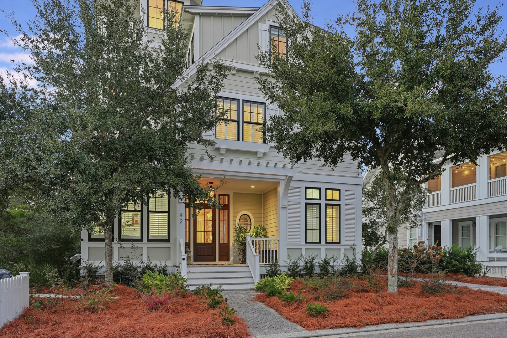 A charming coastal-style home nestled among mature trees with welcoming front entrance and manicured landscaping, located in a peaceful residential neighborhood.