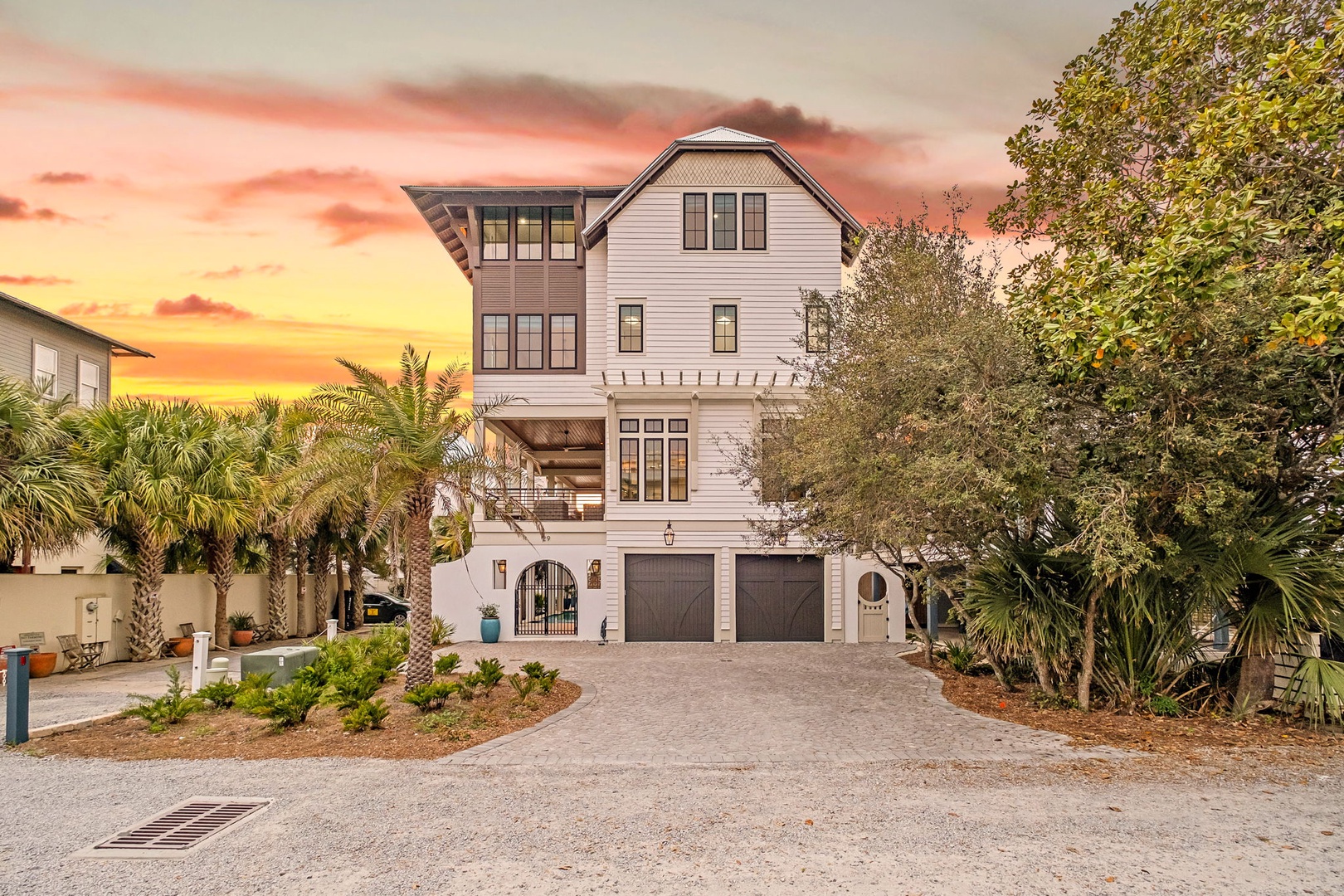 A stunning coastal property with tropical landscaping captures the breathtaking sunset colors painting the evening sky in vibrant coral and gold hues.