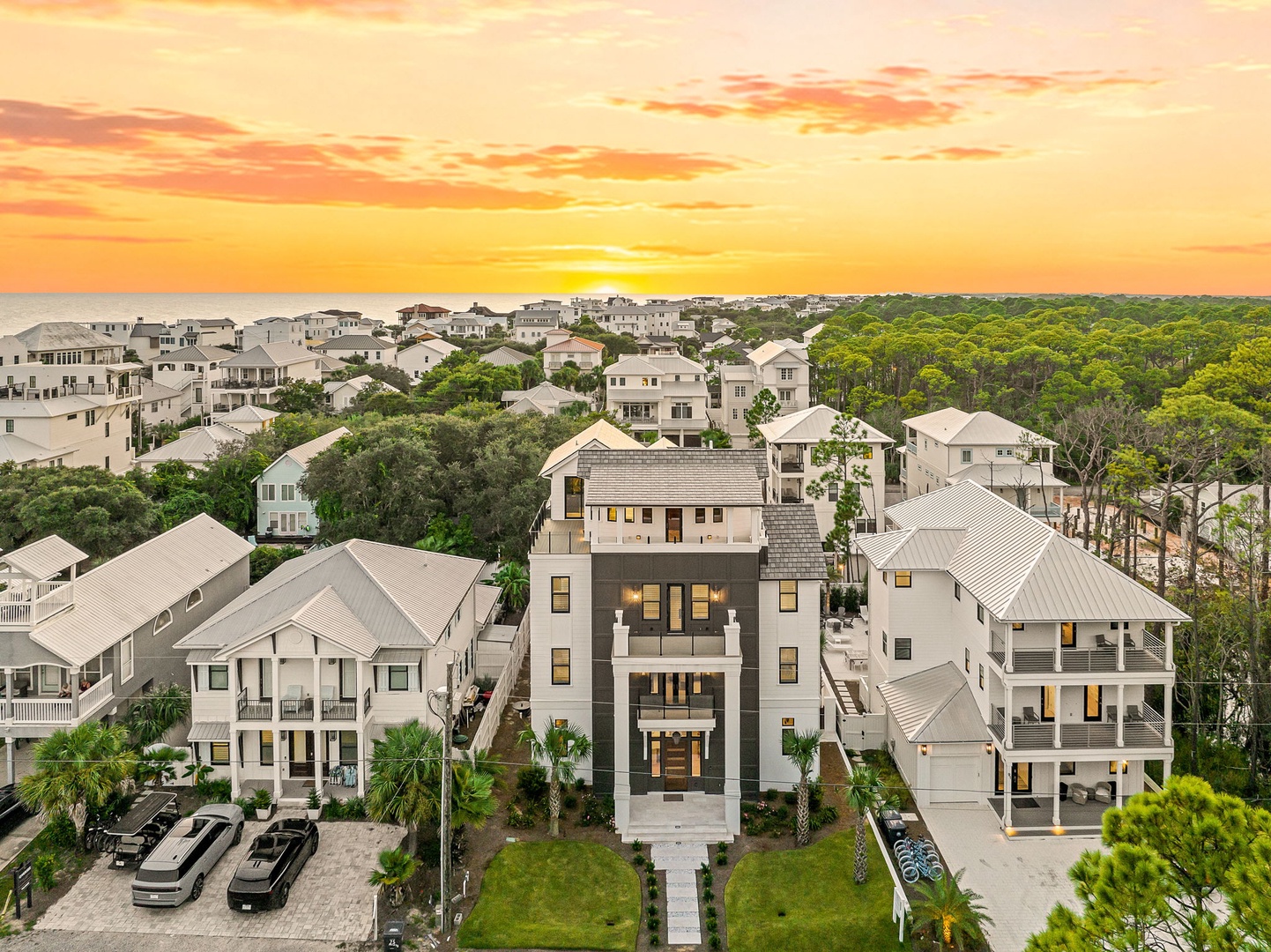 Aerial twilight view of a coastal neighborhood framed by lush forest and glowing evening skies.