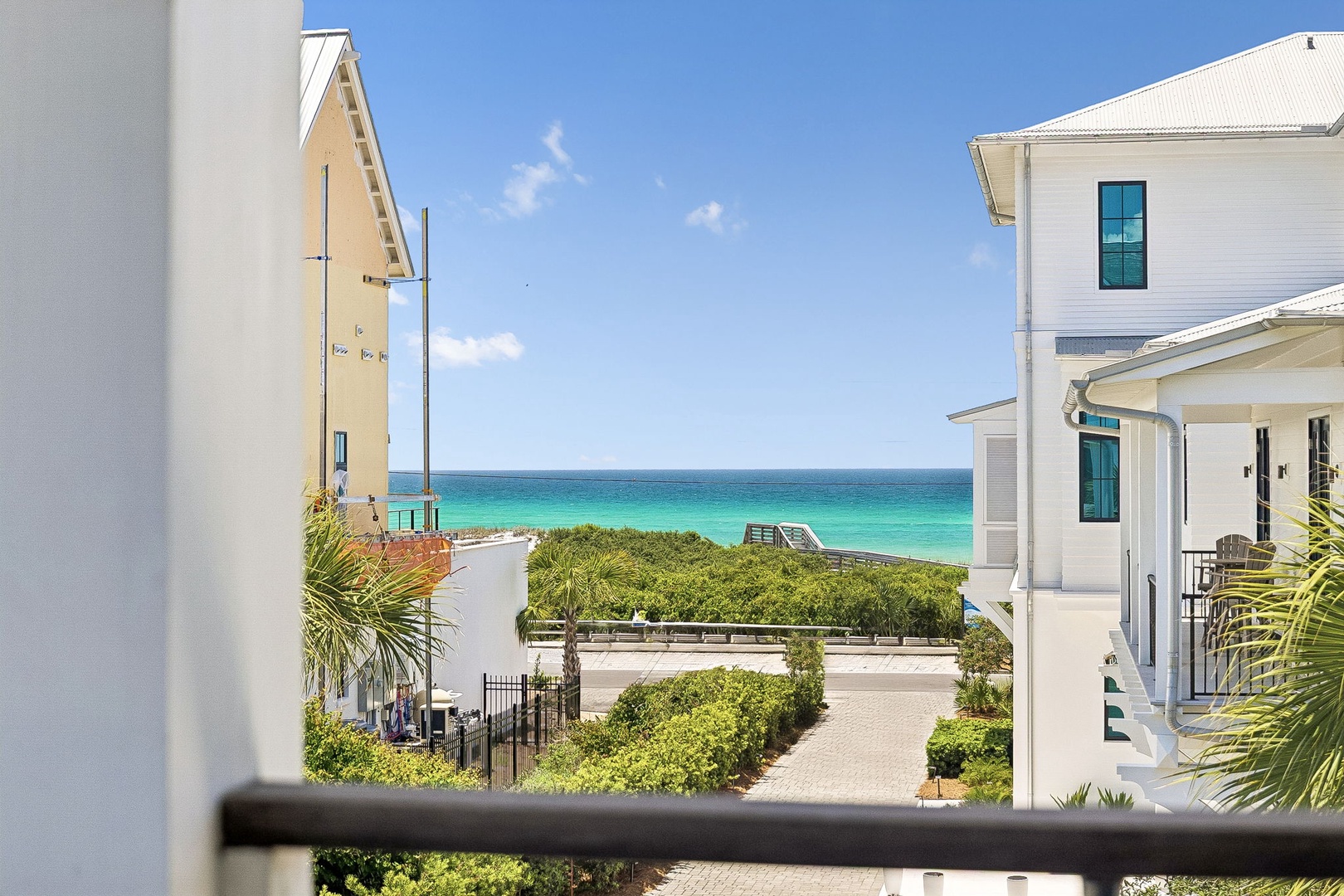 Coastal community setting with turquoise waters and beach access nearby, framed by charming white residential architecture and native dune vegetation.