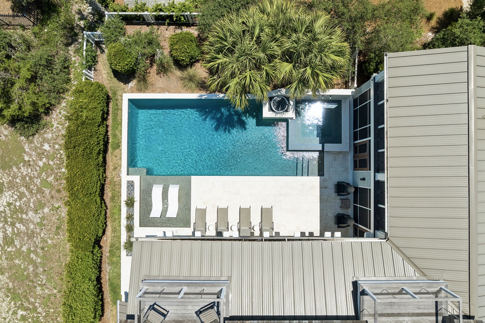 Aerial view of a vacation rental property featuring a pristine swimming pool surrounded by loungers and lush tropical landscaping, providing a serene outdoor retreat.