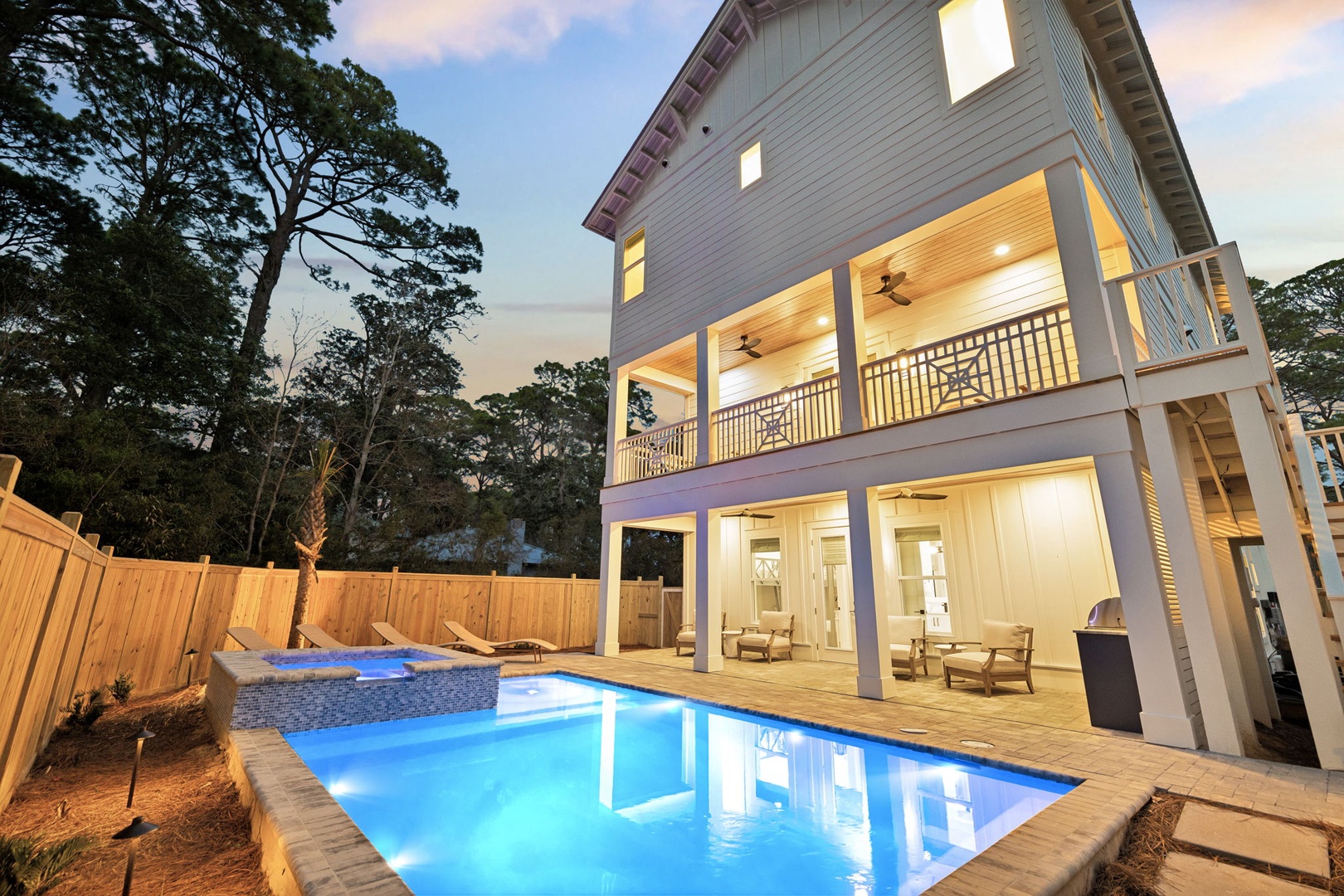 Modern coastal home with private pool surrounded by mature trees and warm evening lighting.