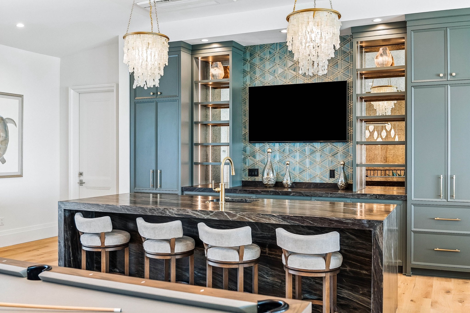 Gather at the sleek marble island in your fully equipped kitchen, where stunning teal tilework and elegant shell chandeliers create an upscale coastal vibe. Your perfect spot for morning coffee or evening cocktails.