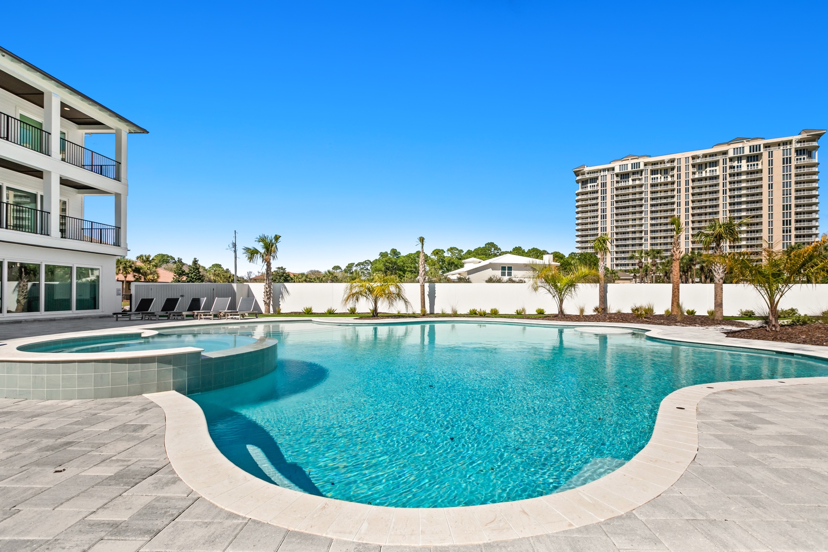 A stunning pool area awaits you with crystal-clear blue water, modern lounge chairs, and lush tropical palms swaying under the Florida sun.