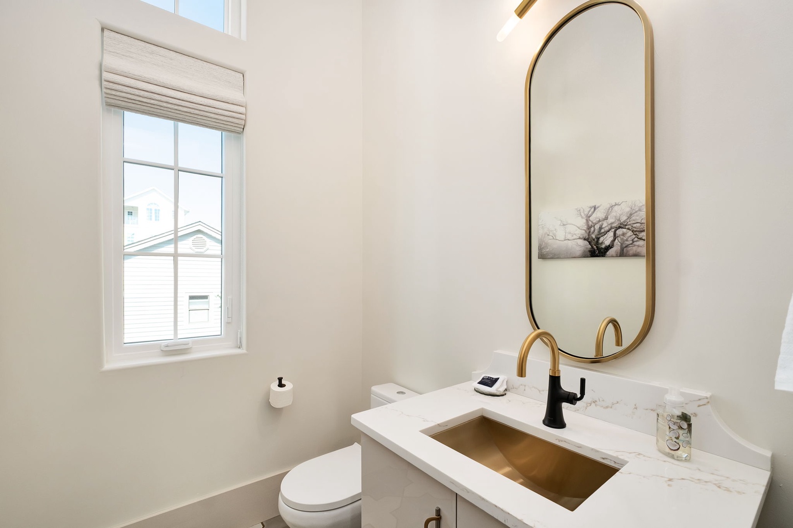 Step into this elegant powder room featuring a stunning brass sink, oval mirror, and marble counters that create a luxurious retreat.