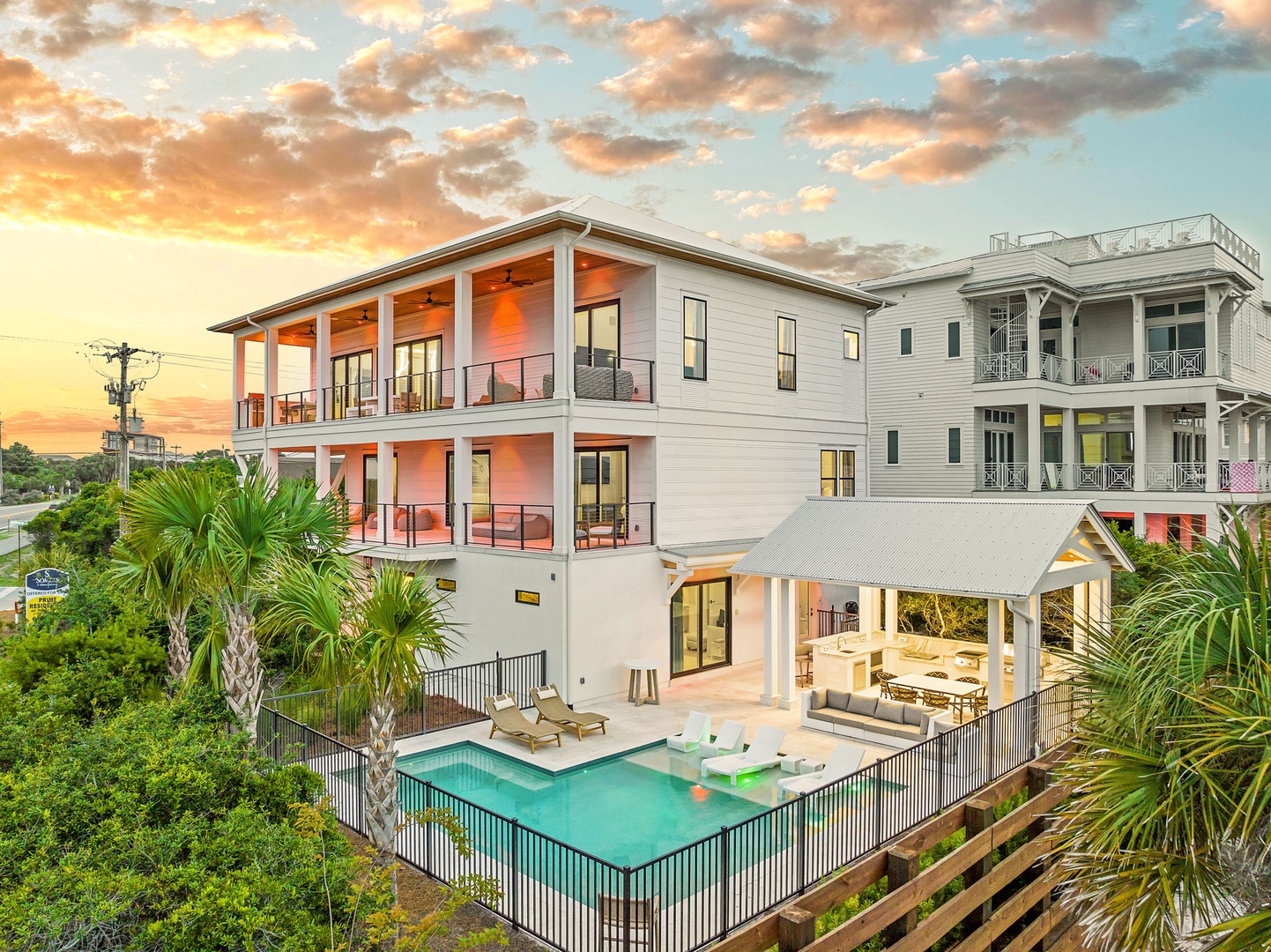 A stunning multi-story vacation home at sunset, featuring a private pool, spacious outdoor entertaining area, and lush tropical landscaping. The property offers modern architecture with multiple balconies perfect for relaxation.