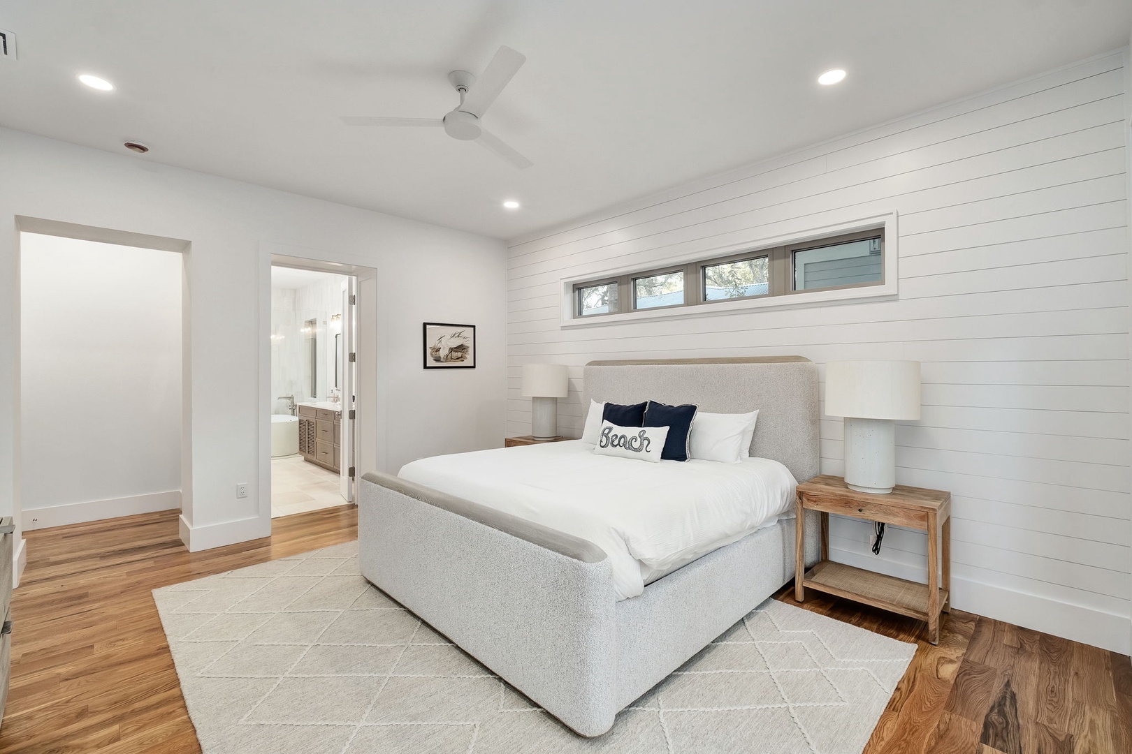 Drift off to sleep in your serene coastal bedroom, where white shiplap walls and warm wood floors create the perfect beachside retreat.