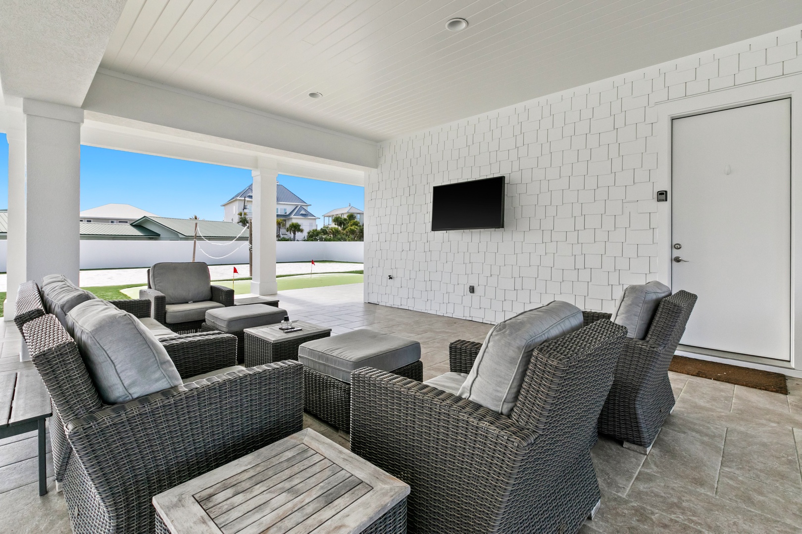 A covered outdoor patio near the property entrance with comfortable wicker seating and a mounted TV, perfect for relaxing while enjoying the view of the surrounding neighborhood.