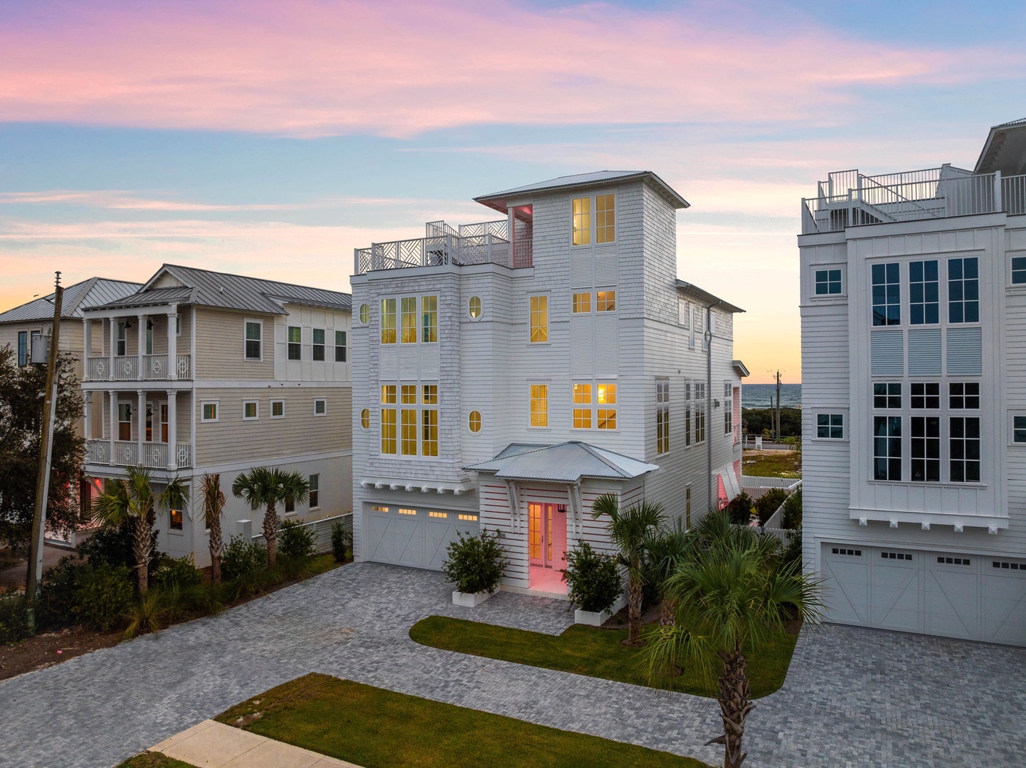 Stunning beachside neighborhood featuring elegant coastal homes with warm lighting against a painted sunset sky.