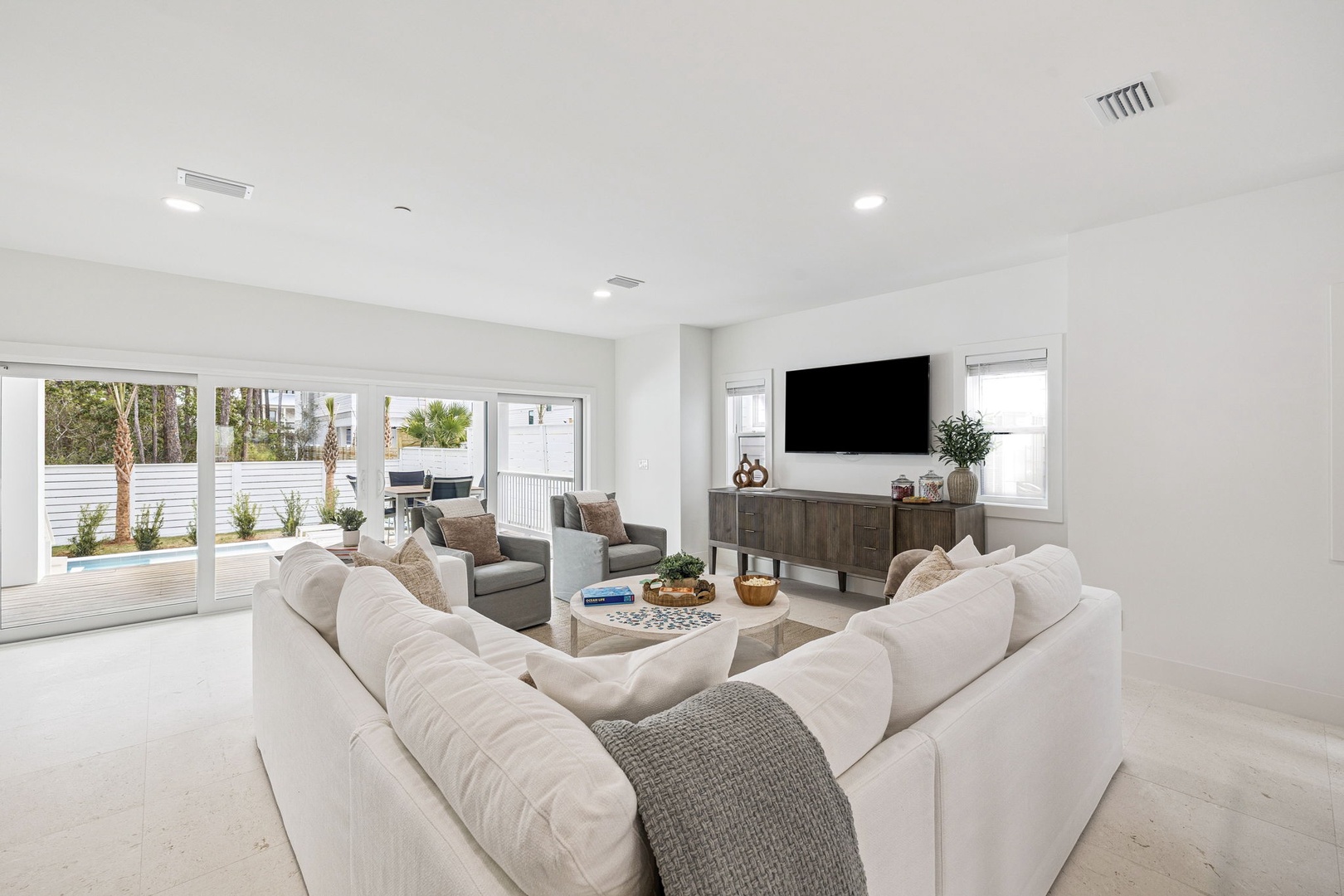 Sink into plush white sofas in this bright, airy living room where natural light flows through floor-to-ceiling windows overlooking your private pool.