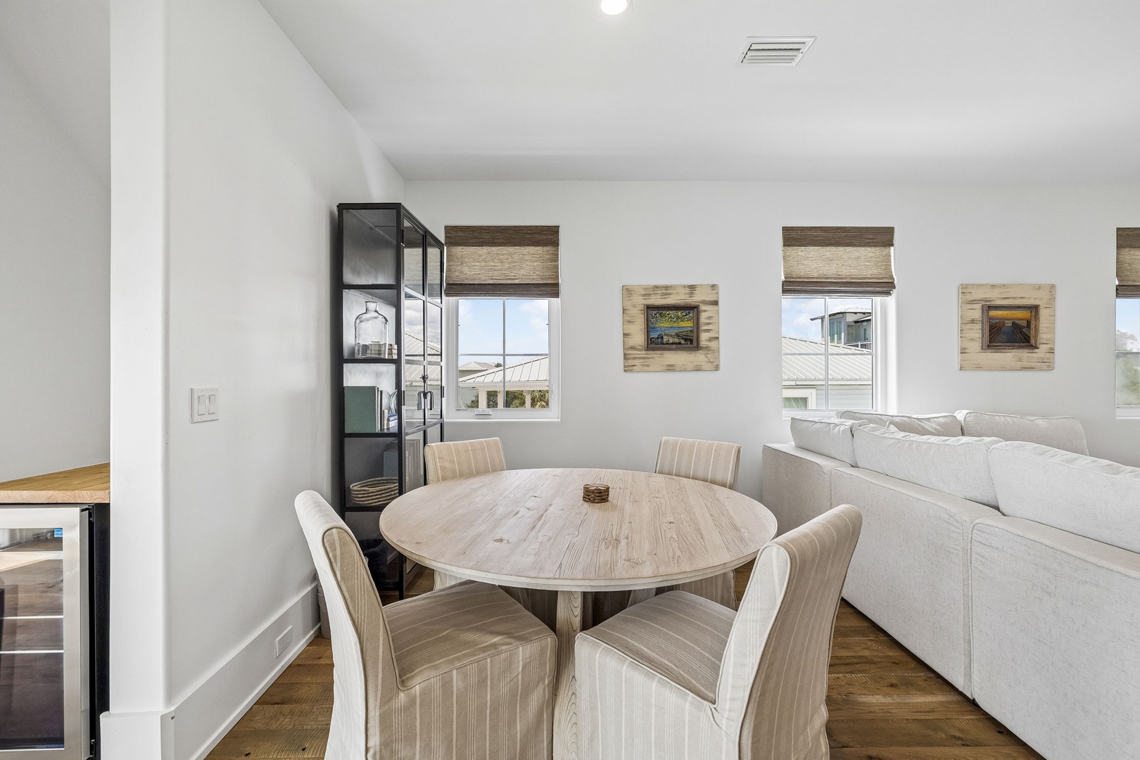 Gather around this inviting round dining table for meals and conversation, where soft natural light and coastal-inspired decor create a warm, airy atmosphere perfect for your stay.