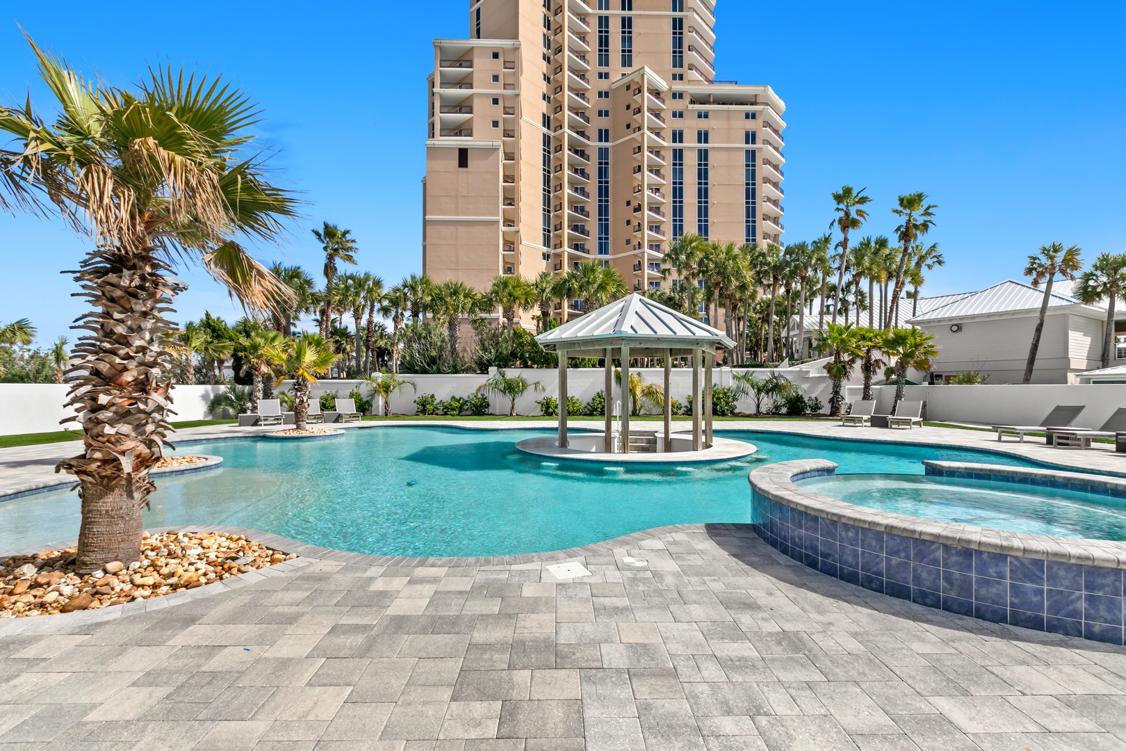 A stunning resort-style pool area surrounded by lush palm trees and tropical landscaping, with a charming gazebo perfect for relaxing in the shade.