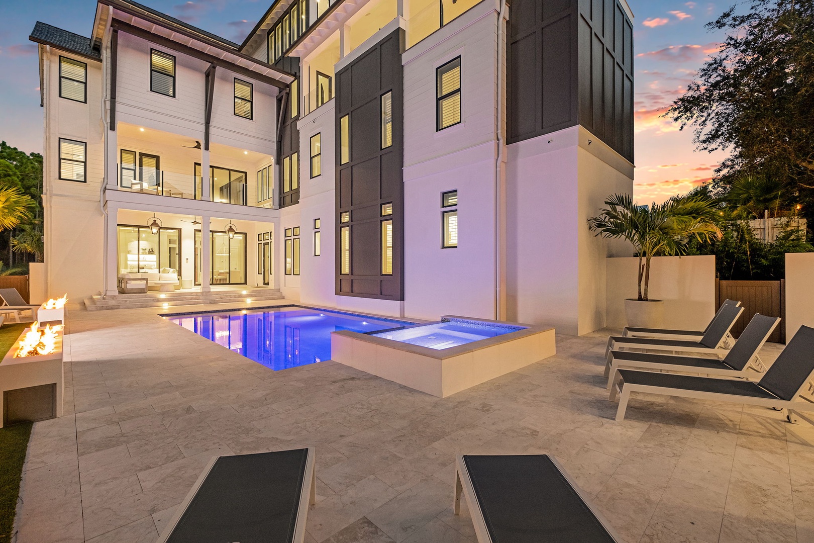 A striking contemporary residence featuring a luxurious pool with spa and spacious patio area, photographed during a vibrant sunset.