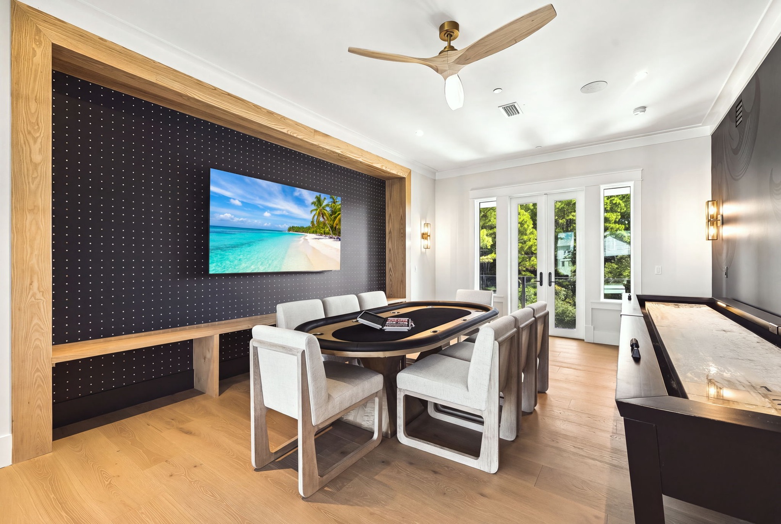 A stylish game room awaits your friendly competitions, featuring a custom poker table and sleek shuffleboard. Natural light flows through French doors while ceiling fans keep you cool during intense matches.