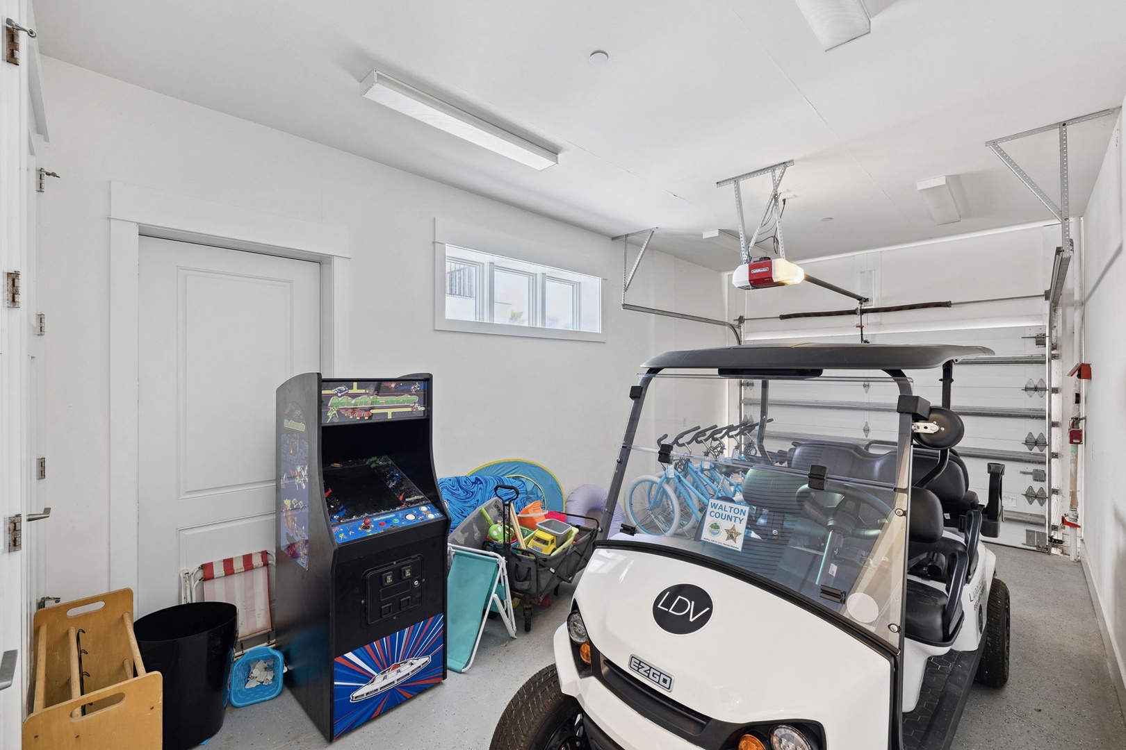 Your entertainment awaits in this spacious garage with classic arcade games, beach gear, and convenient golf cart access for exploring.