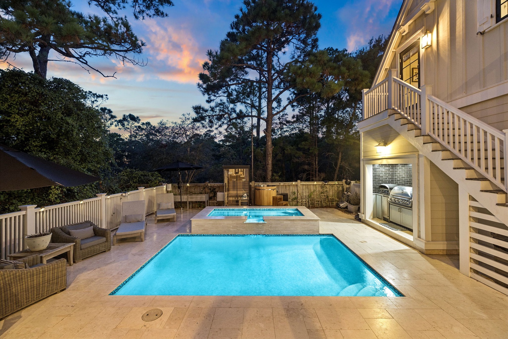 A stunning outdoor space features a sparkling pool and hot tub, surrounded by comfortable lounge seating and an outdoor kitchen—perfect for relaxing evenings under softly glowing lights as the sky paints dusk colors overhead.