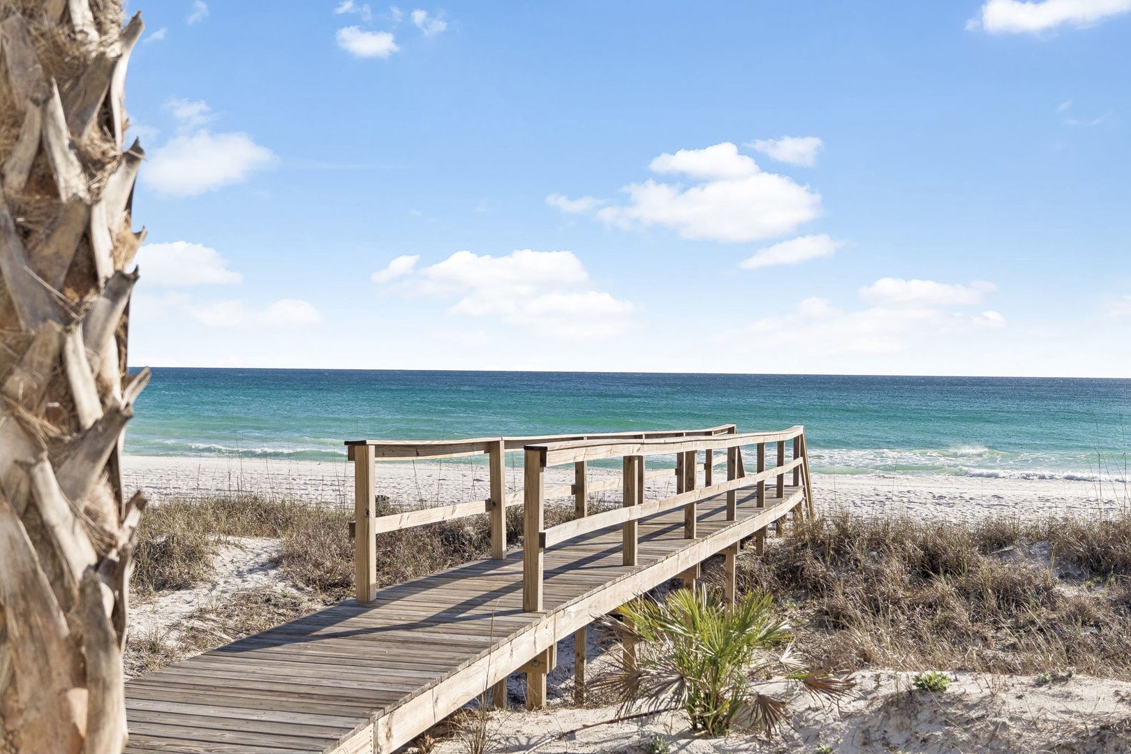 Pristine beach access awaits with turquoise waters and white sand visible from the property's wooden boardwalk pathway.