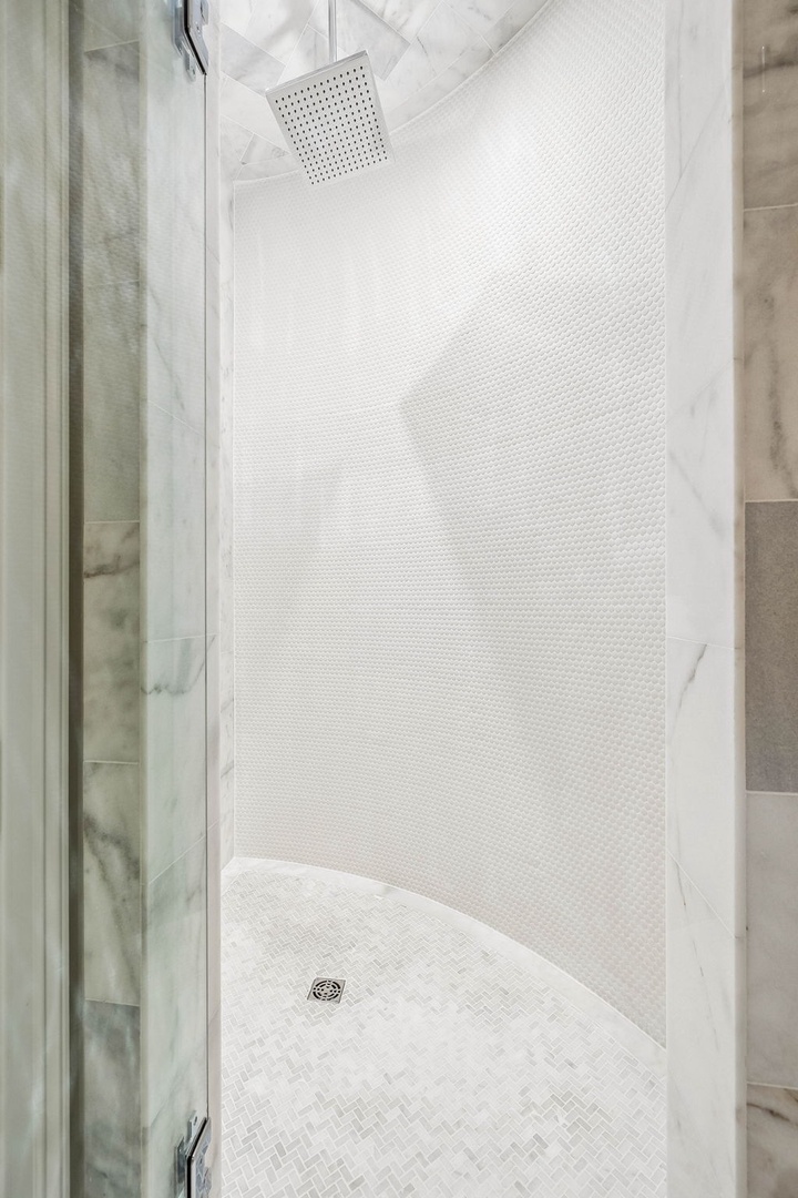 Your private spa-style shower features a rainfall showerhead and elegant white tile, creating a serene space to start your mornings refreshed.