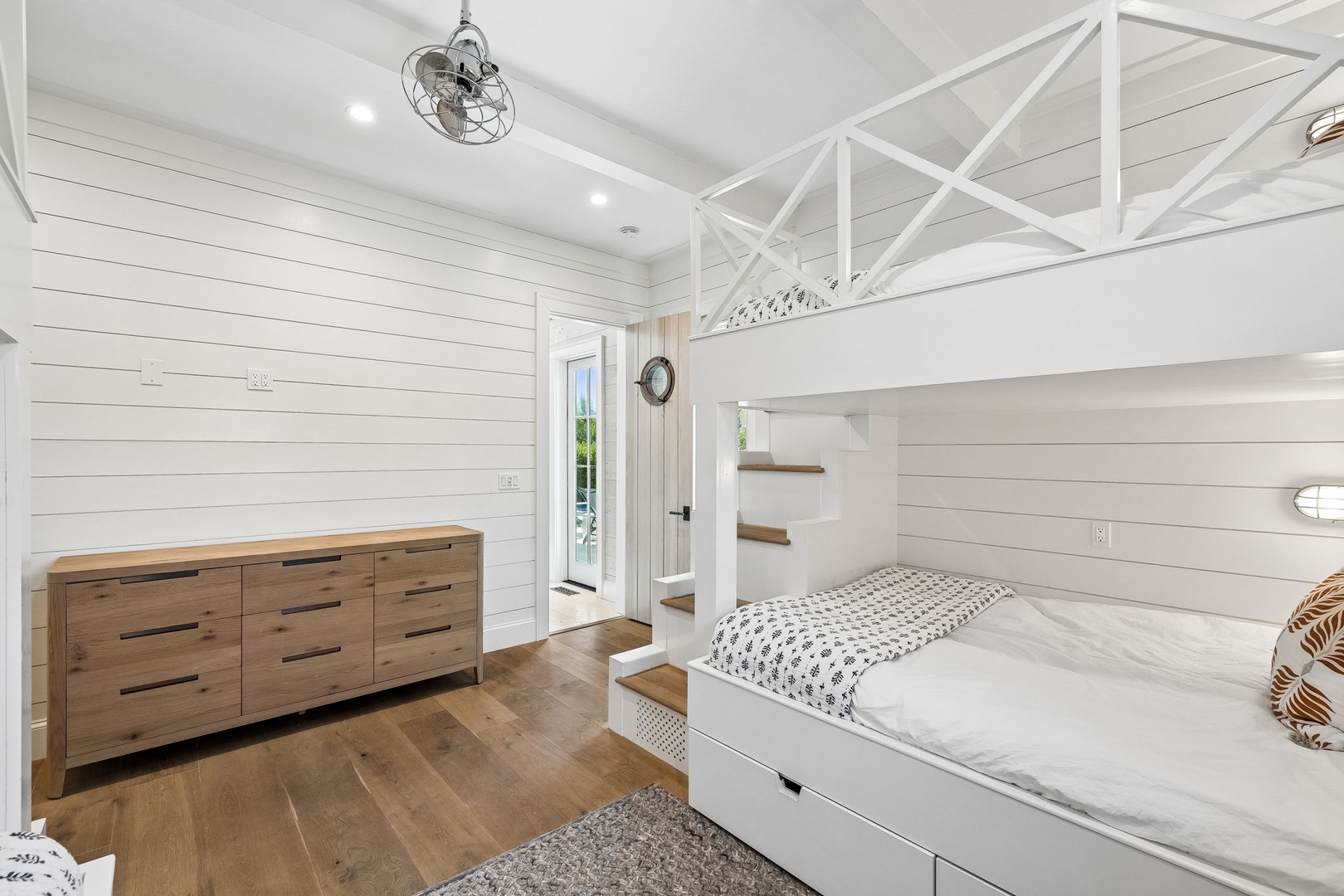 Your space features a cozy bunk bed, warm wood floors, ample storage, and natural light streaming through French doors—perfect for restful nights and relaxed mornings.