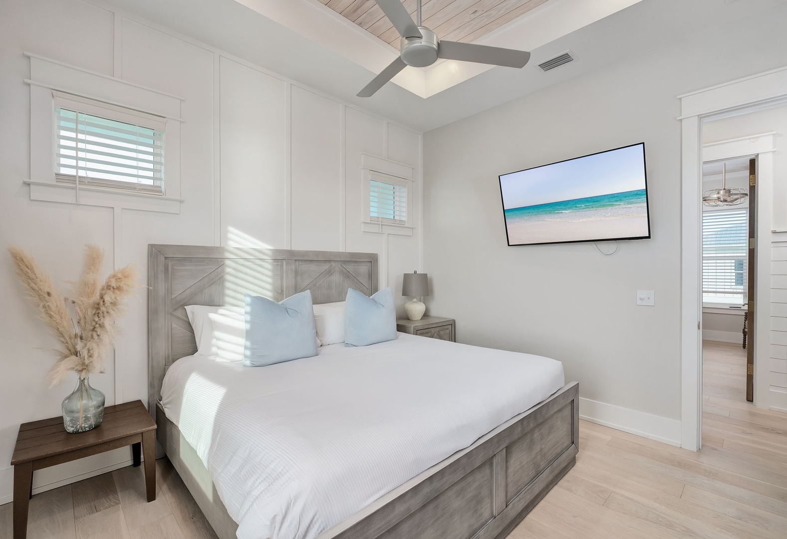 Your serene bedroom features crisp white linens, coastal blue accents, and beach views on the wall-mounted TV for ultimate relaxation.