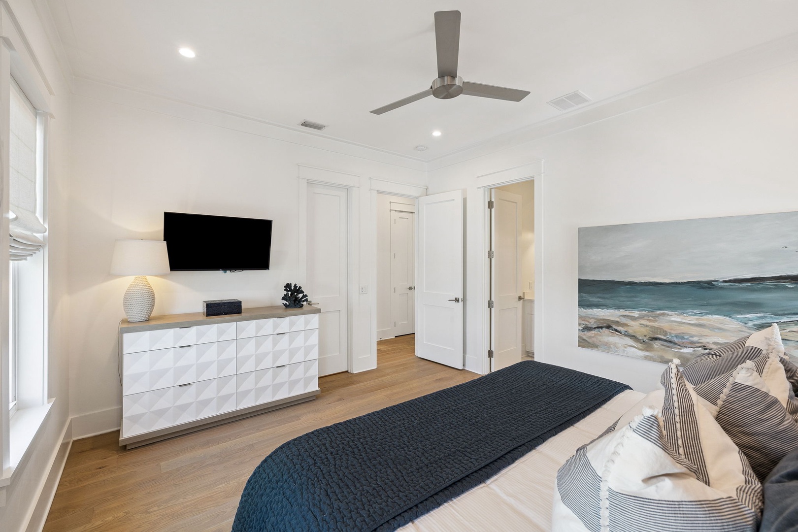 Drift off to sleep in your serene bedroom featuring coastal artwork, modern amenities, and a ceiling fan for perfect comfort.