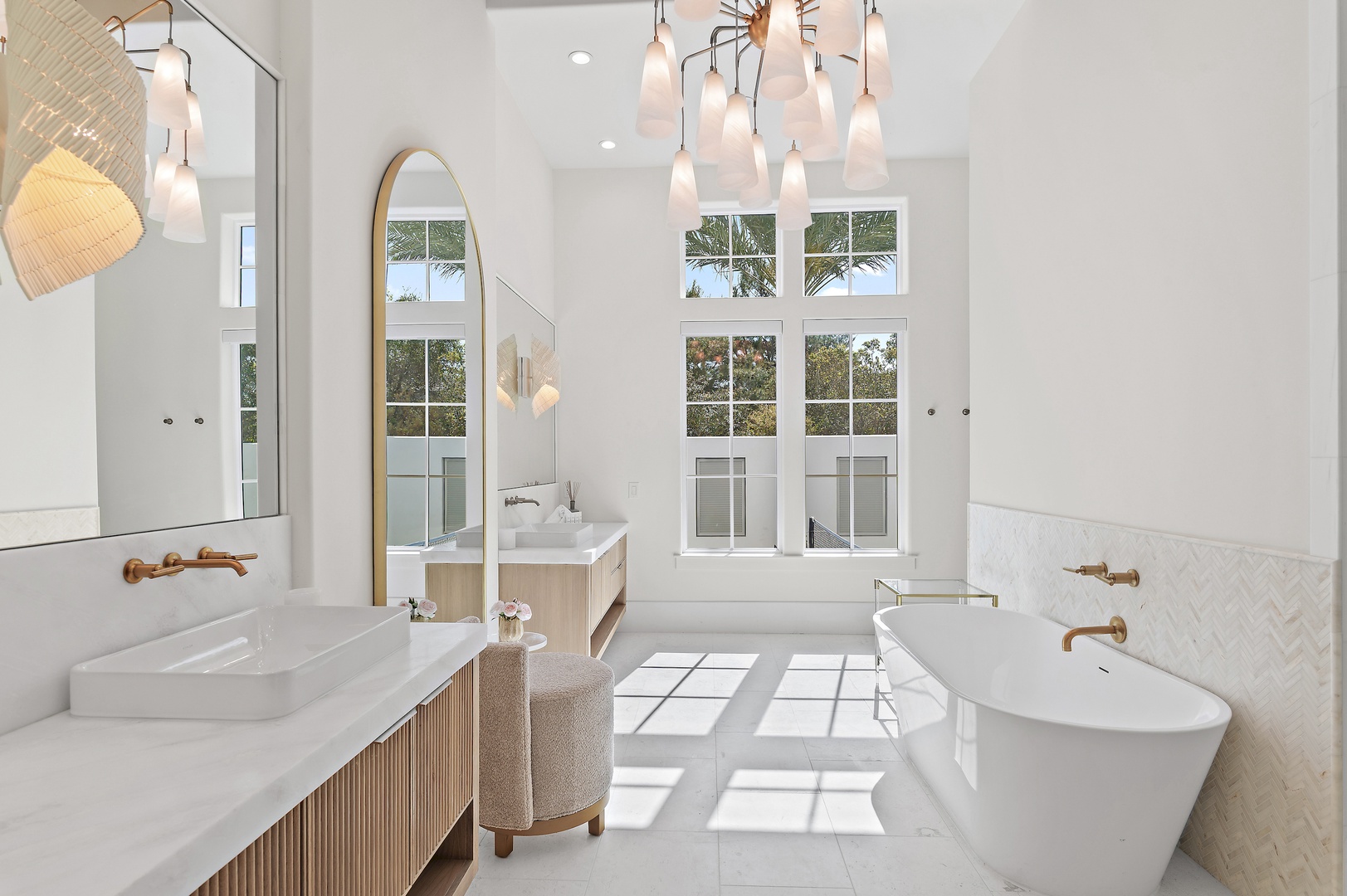 Soak in the freestanding tub surrounded by elegant white herringbone tile, warm wood accents, and natural light pouring through tall windows—your private spa retreat awaits.