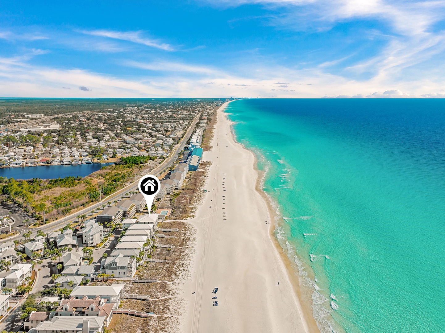 Aerial view of a beachfront vacation rental property situated along pristine turquoise waters and white sandy shores, with easy access to the coastal road and nearby amenities.